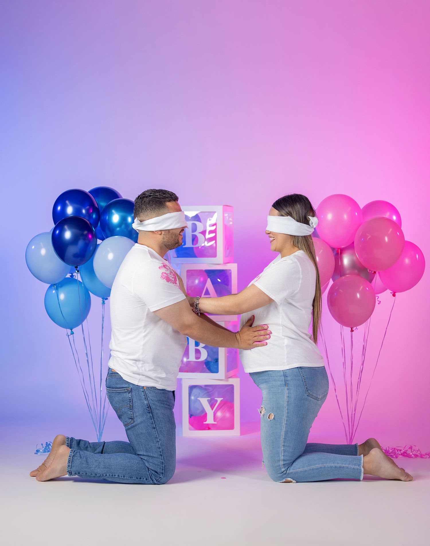 Blindfolded couple kneeling at gender reveal with BABY boxes and balloons.