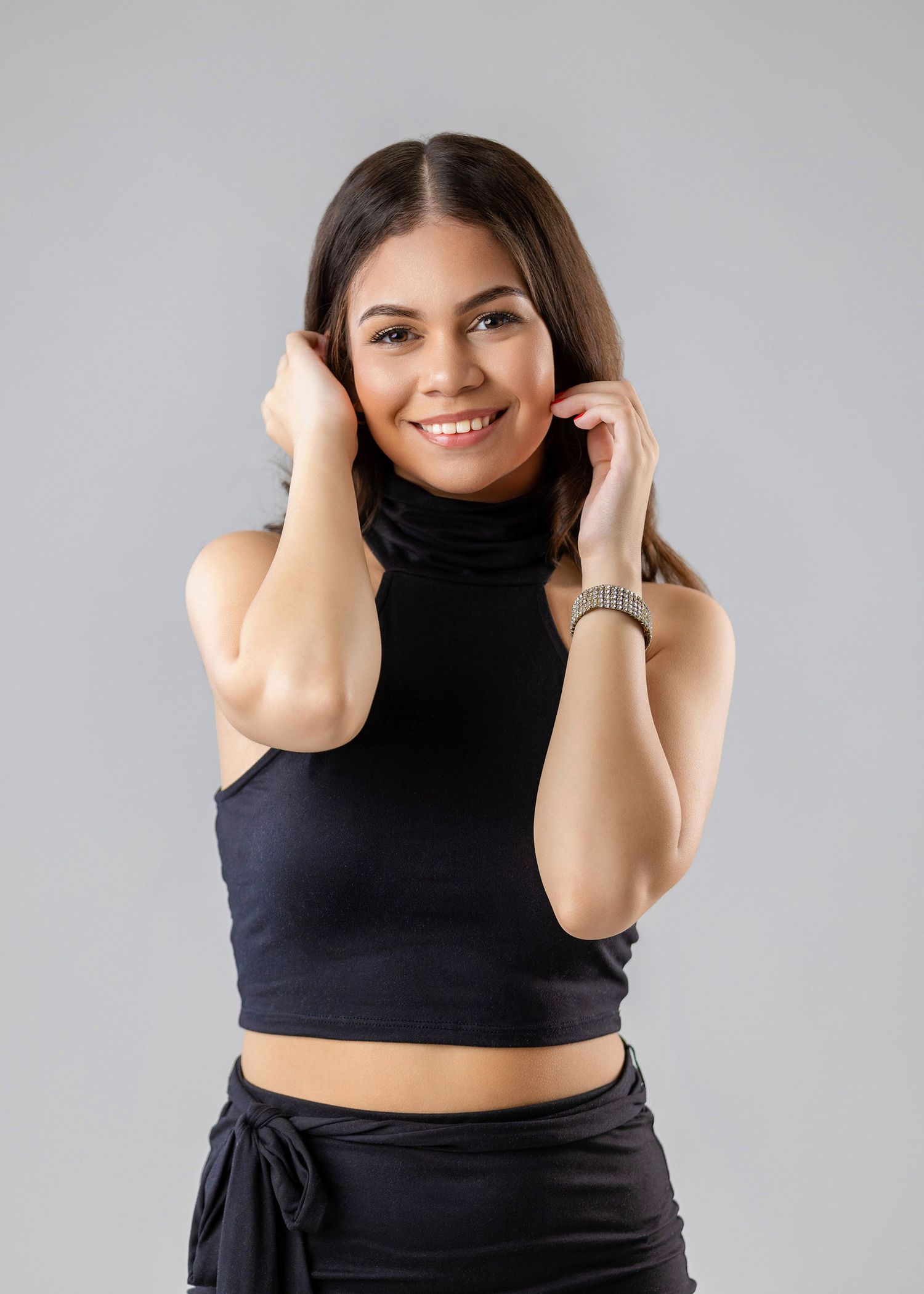 Young woman in black turtleneck crop top smiling against gray studio background.