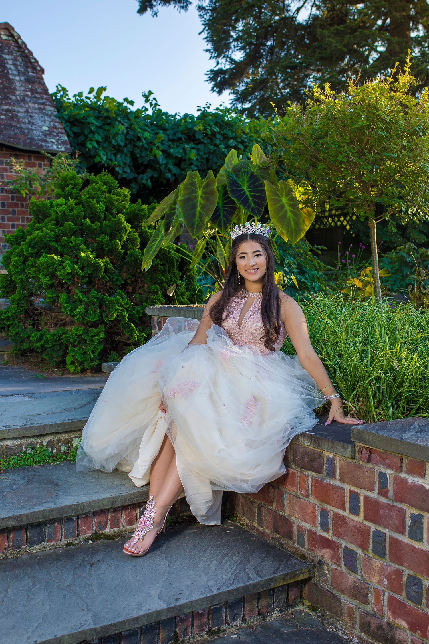 A flowing white gown draped elegantly across brick steps in a lush garden setting during a photo session.