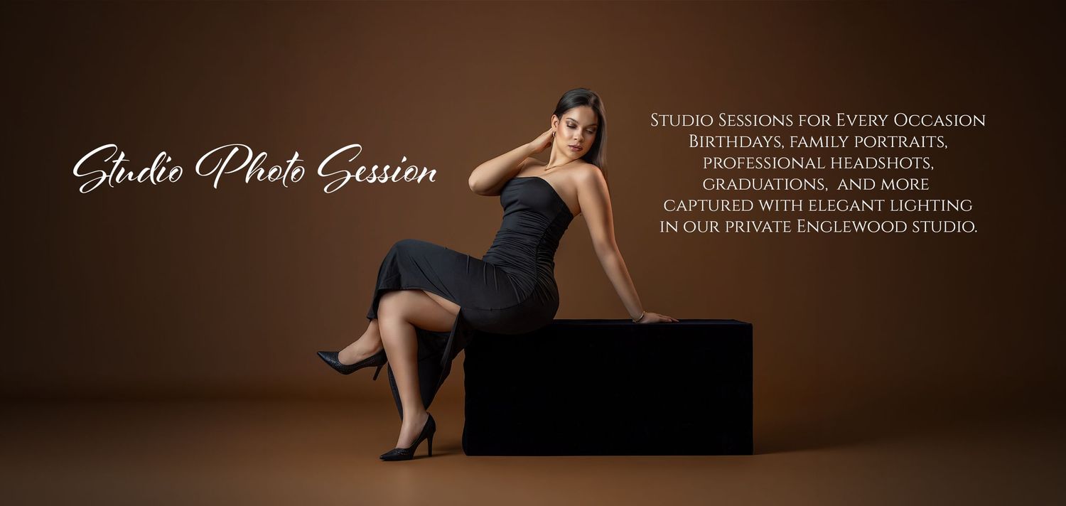 A woman in an elegant black dress poses gracefully in a professional studio photo session with warm lighting.