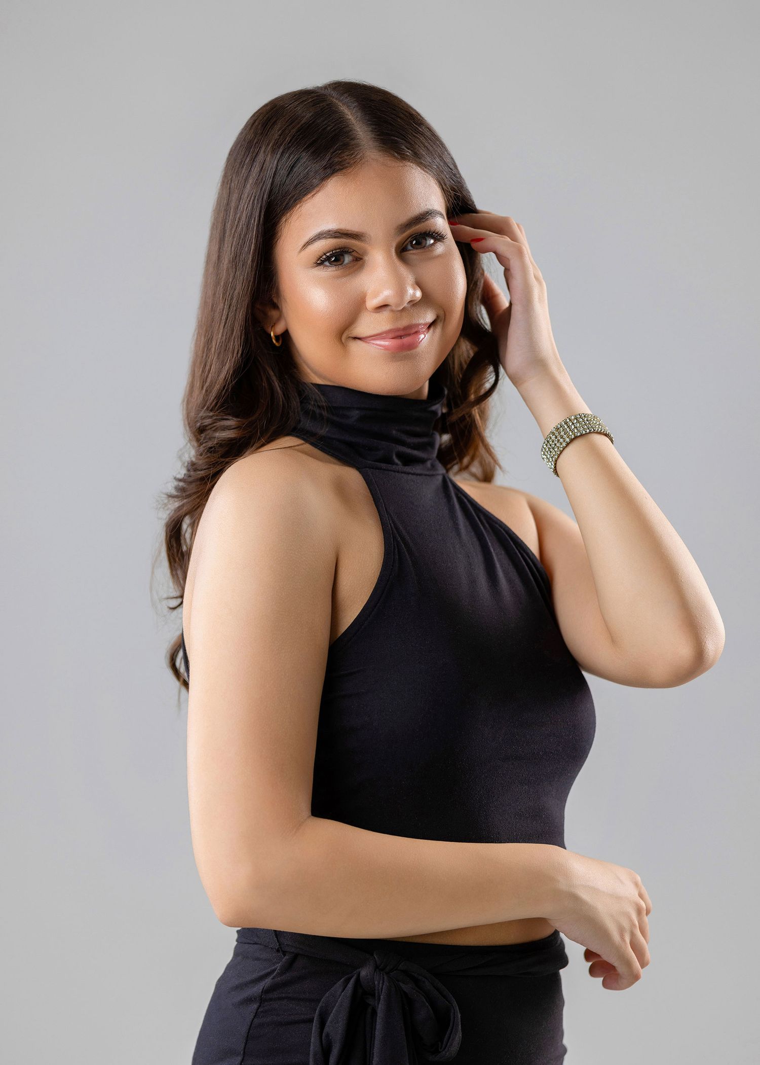 Young brunette woman smiling in black turtleneck crop top against light gray background.