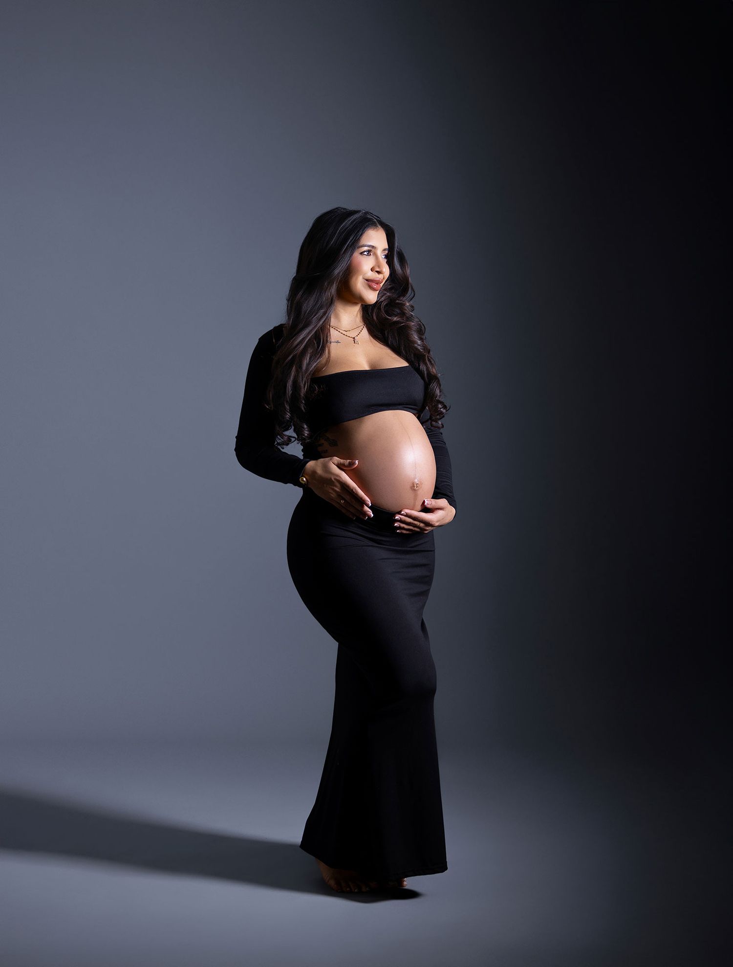 Dramatic maternity silhouette series in black dress against dark studio backdrop.