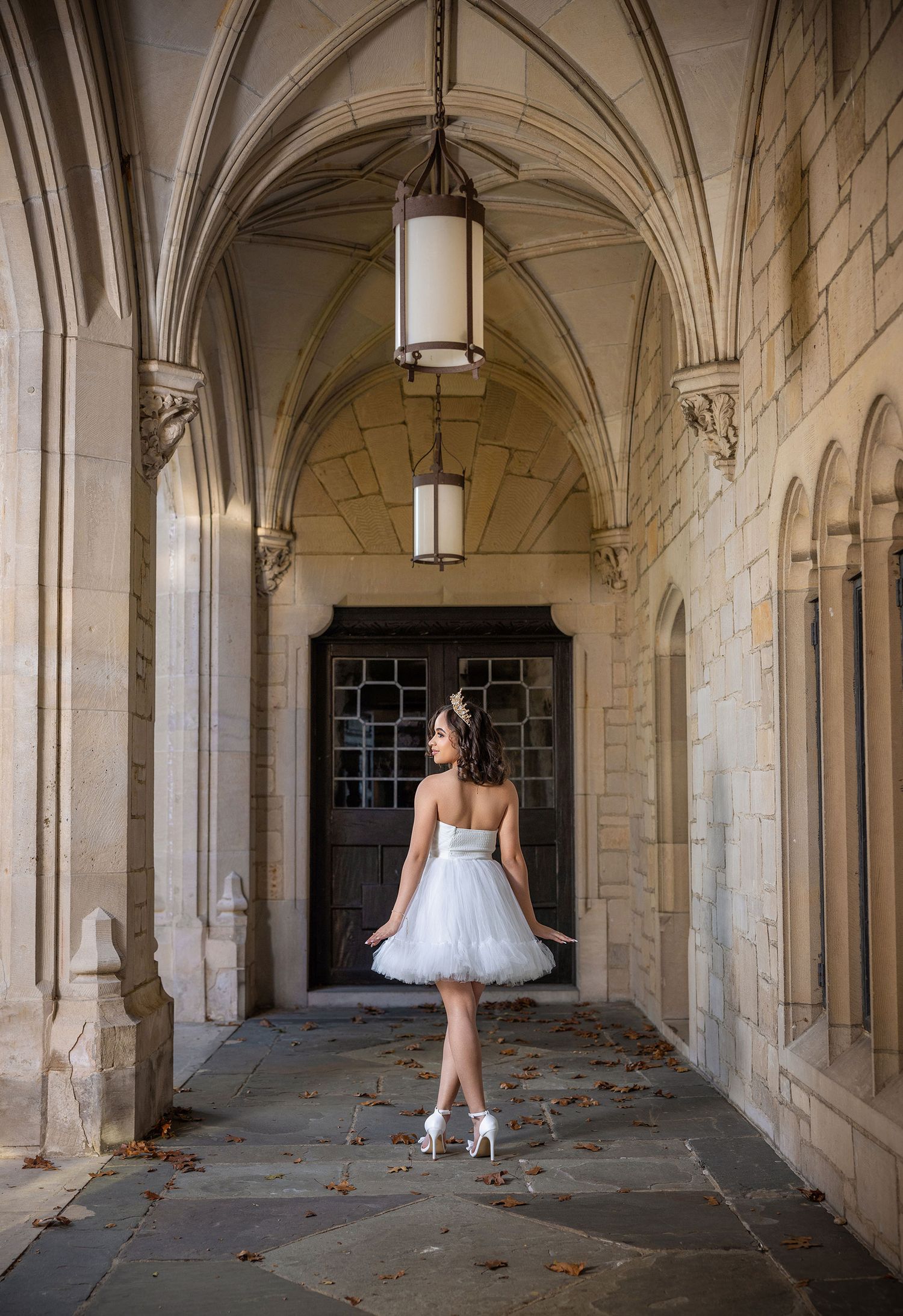 A ballerina in a white tutu dances through a historic stone archway corridor with dramatic lighting and shadows.