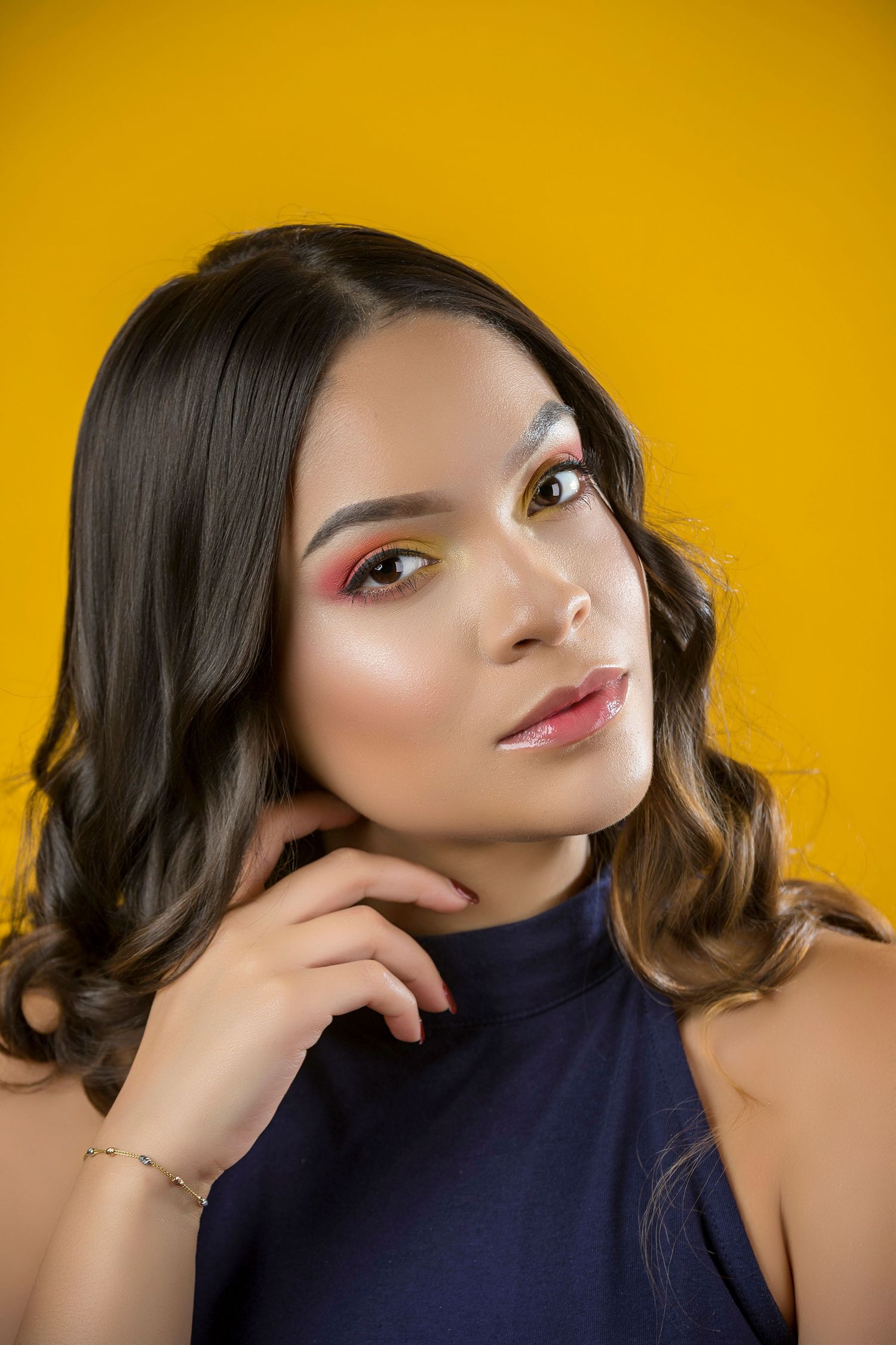 Young woman with colorful eye makeup and wavy hair posing against yellow background.