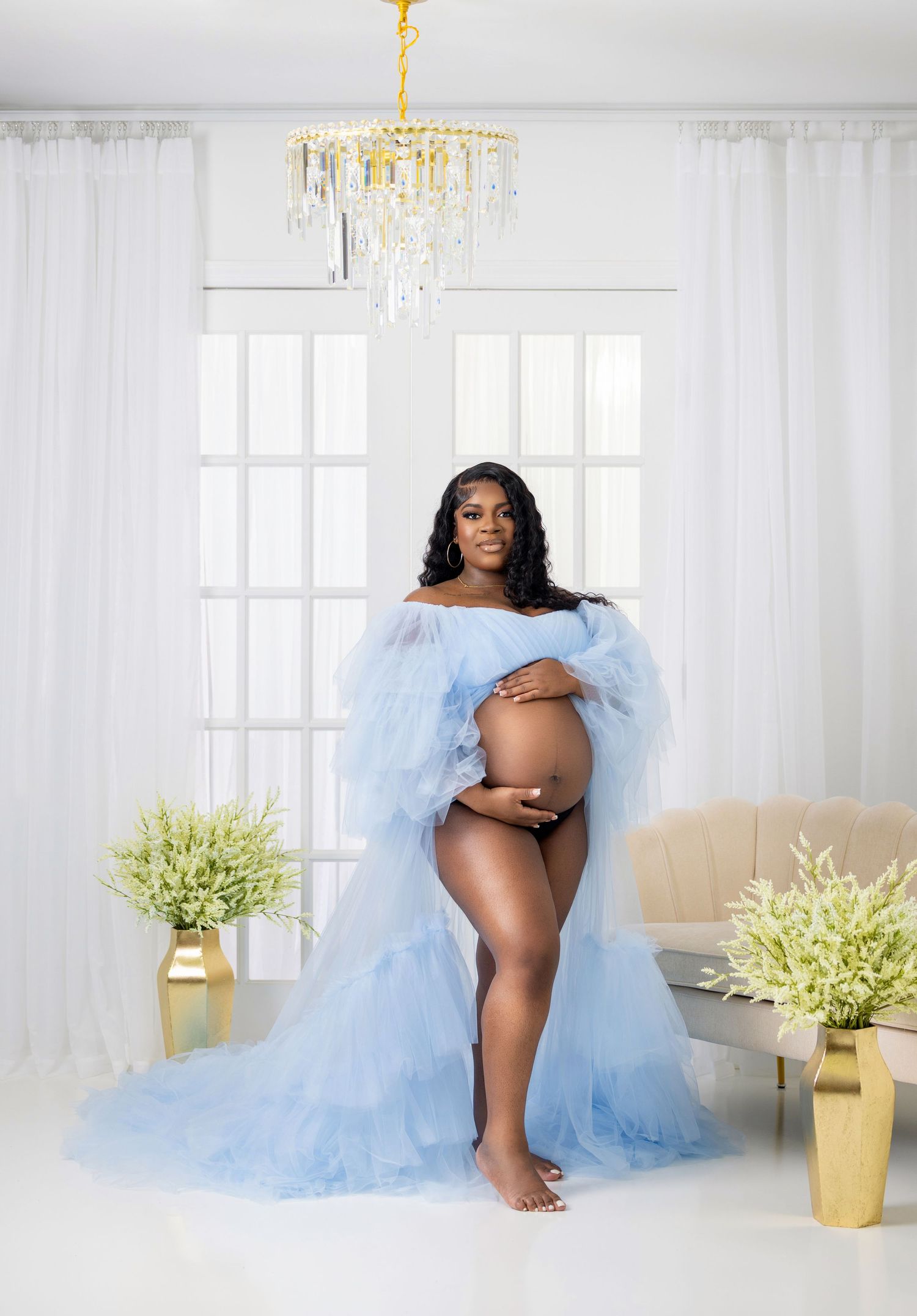 A maternity photoshoot in a bright white room with elegant decor featuring a flowing light blue tulle gown.