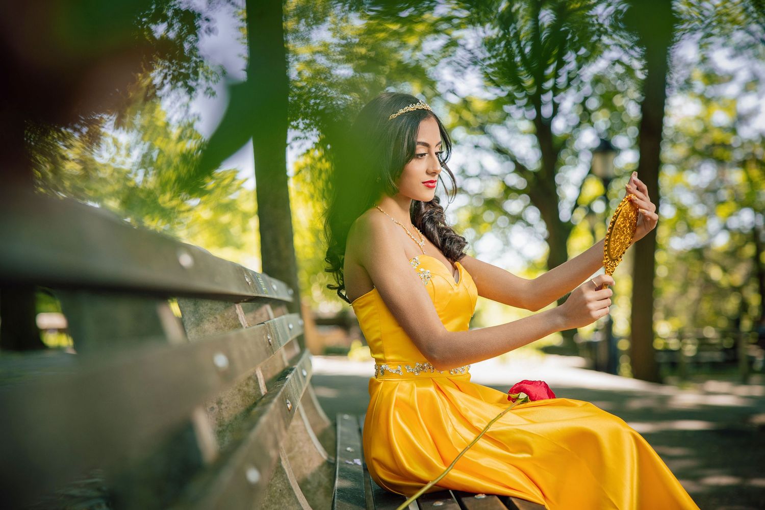 A person in a bright yellow dress poses in a sunlit outdoor garden setting with lush greenery.