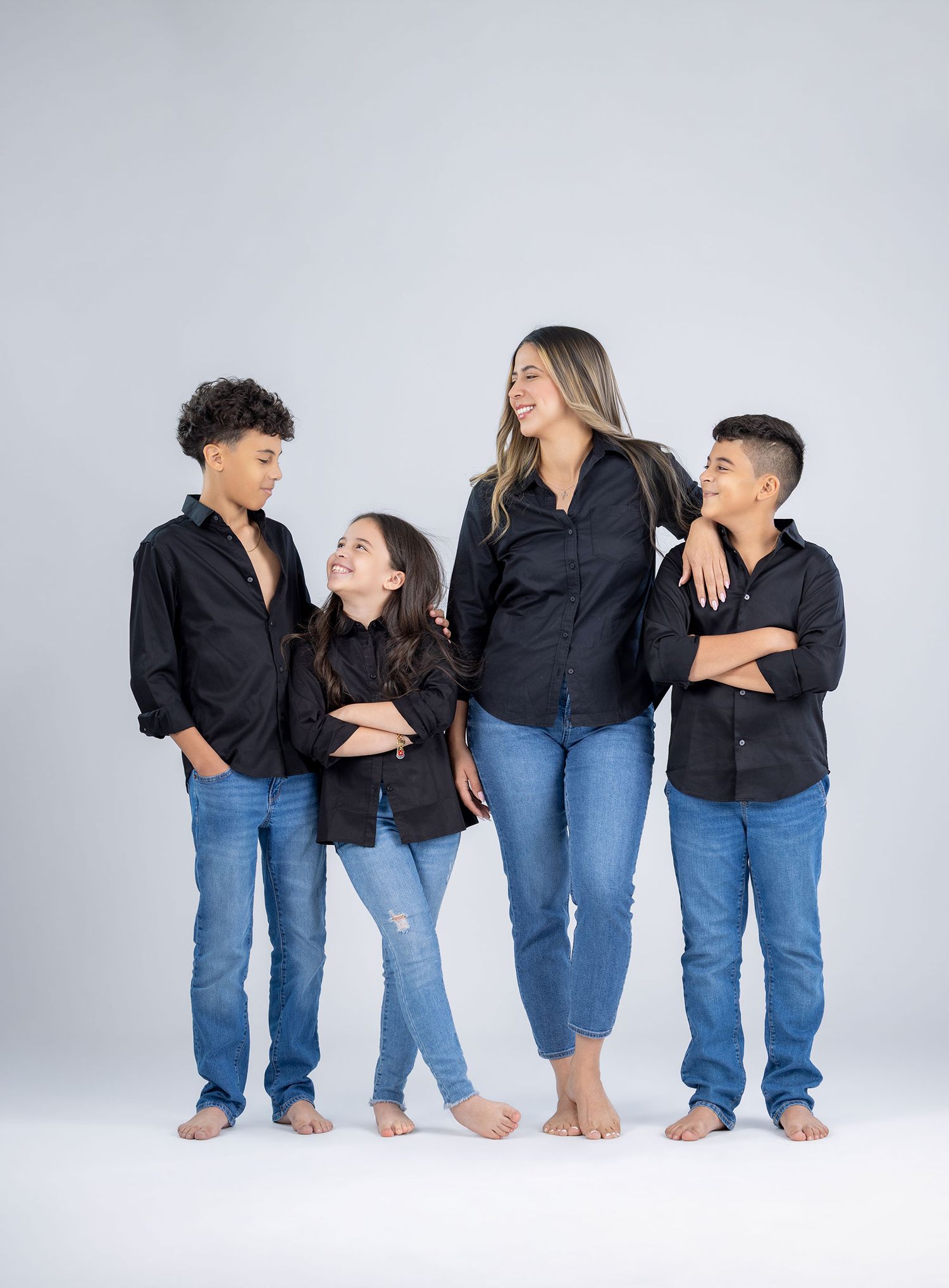 Mother and three children in matching black shirts and jeans pose together.