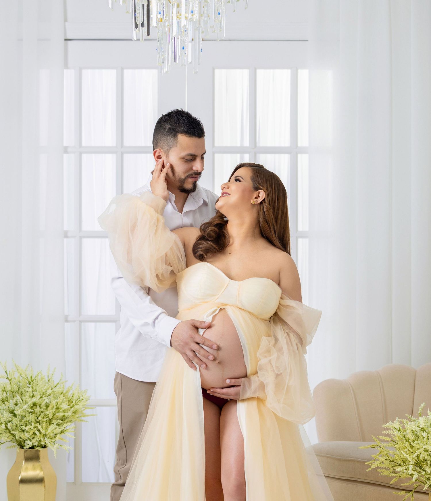 Couple in yellow and white outfits dancing together in a bright modern living room with decorative plants.