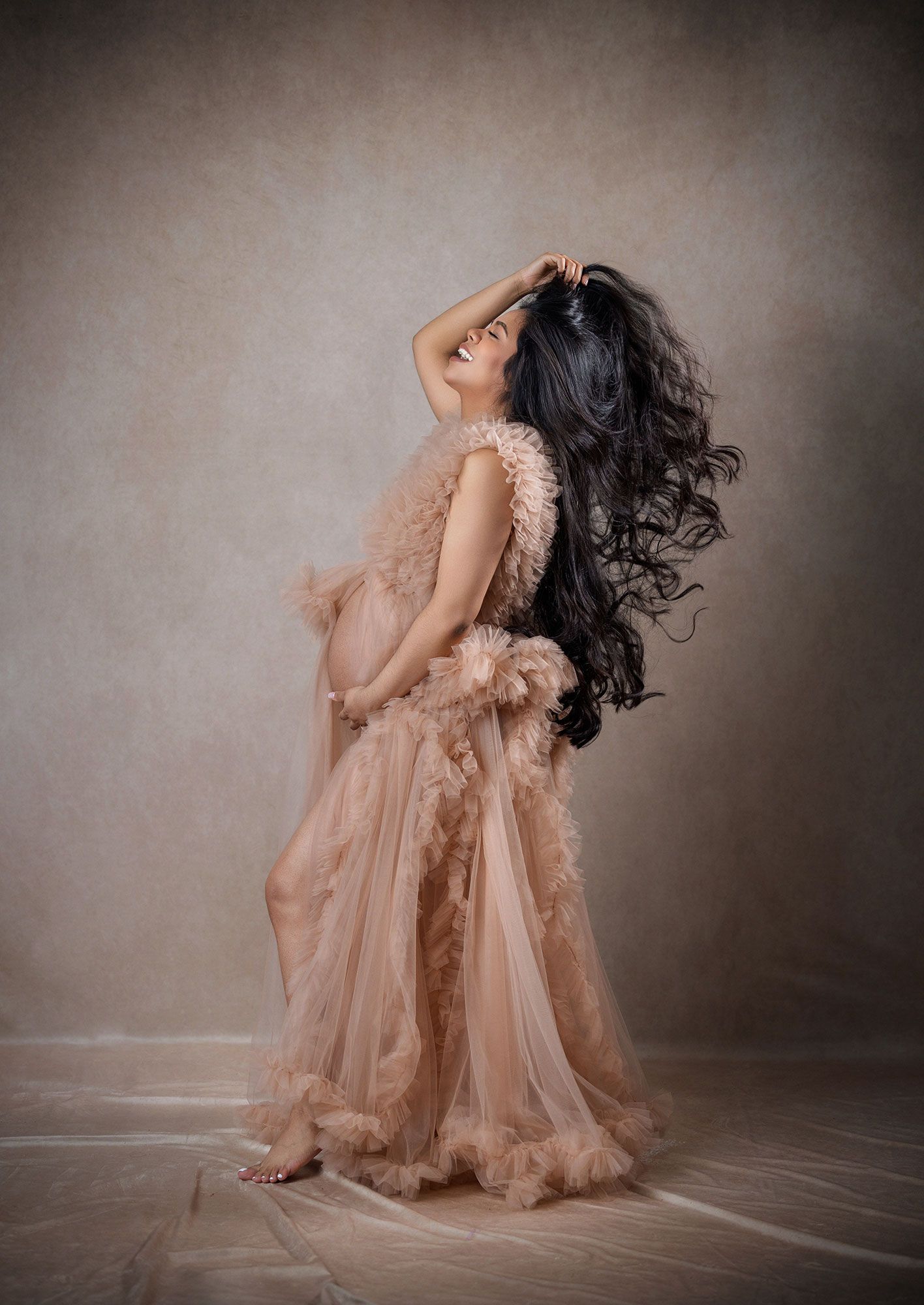 Ethereal maternity portraits featuring flowing peach gown and dramatic poses in studio setting.