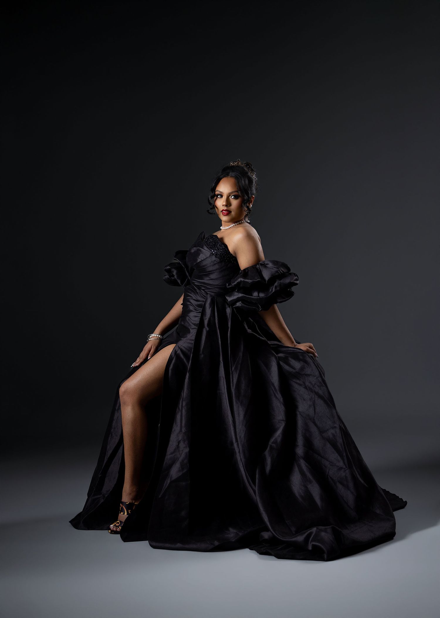Woman in dramatic black ruffled ball gown poses gracefully against dark studio background.