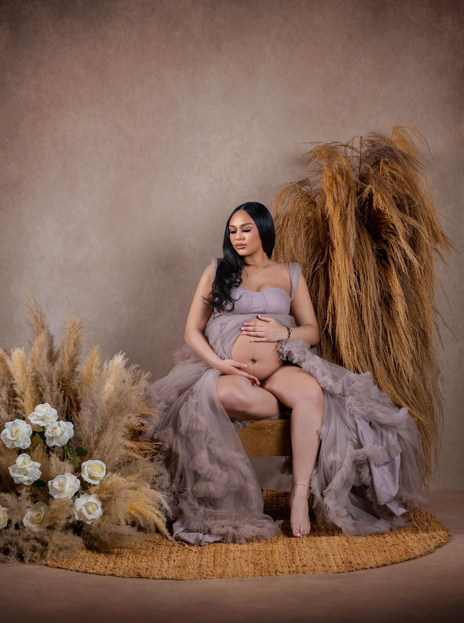 Romantic maternity session with pampas grass, roses and flowing mauve dress against neutral background.