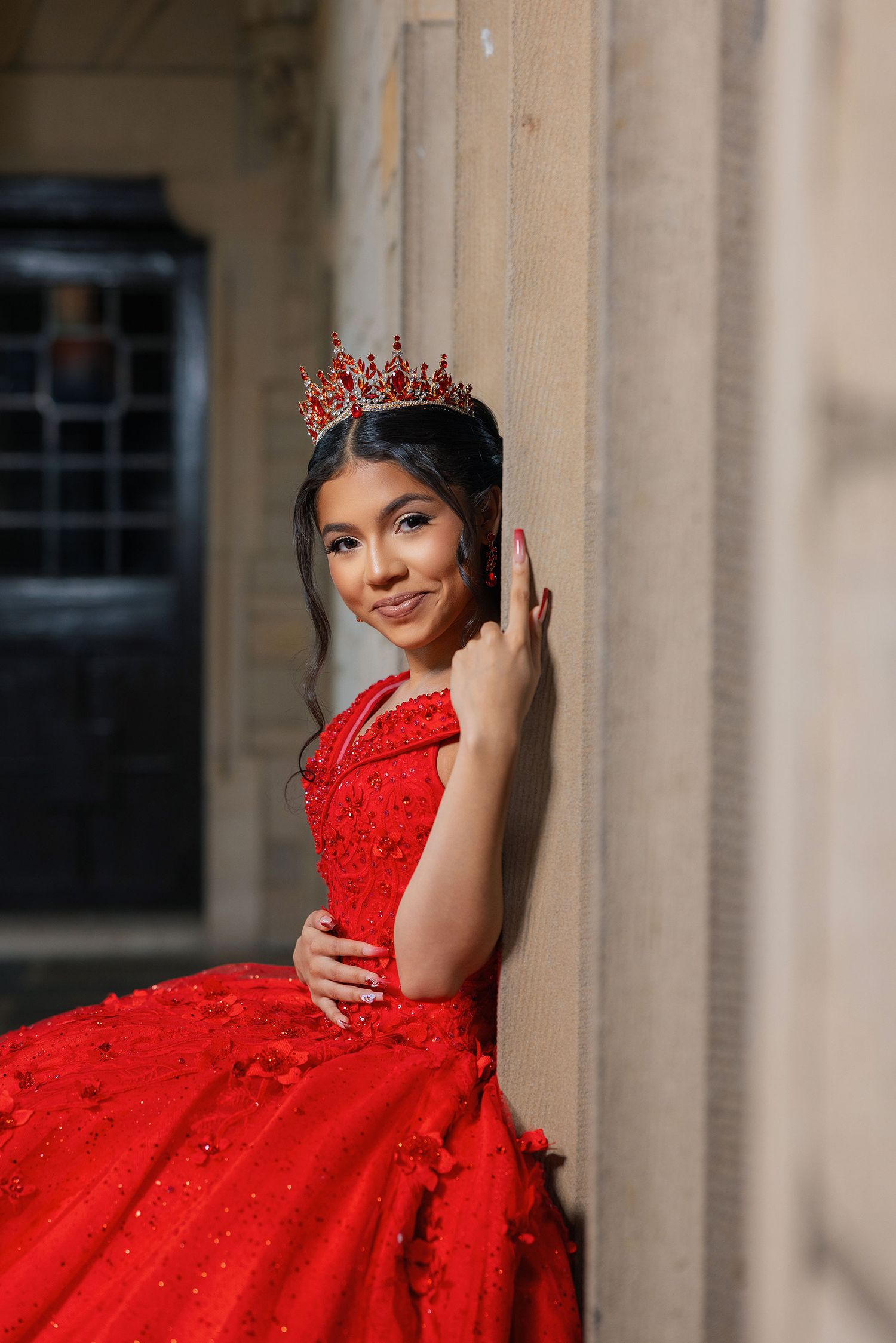 A vibrant red formal gown with intricate beading and lace details photographed against stone columns.