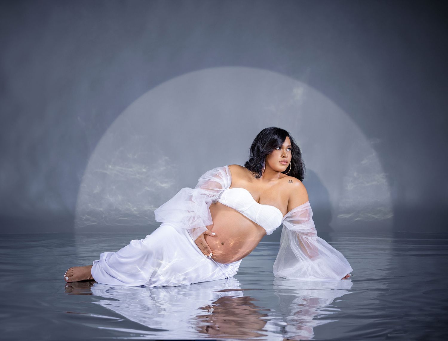 A figure in a flowing white dress poses gracefully in dark water creating an ethereal and artistic composition.