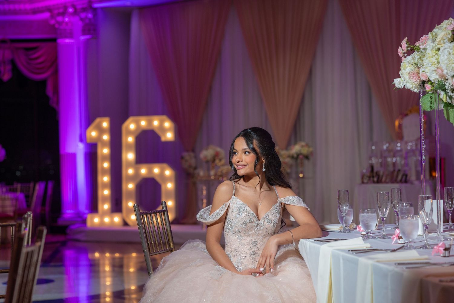 Wedding reception venue decorated with purple uplighting, white drapes, and elegant table settings for a formal celebration.