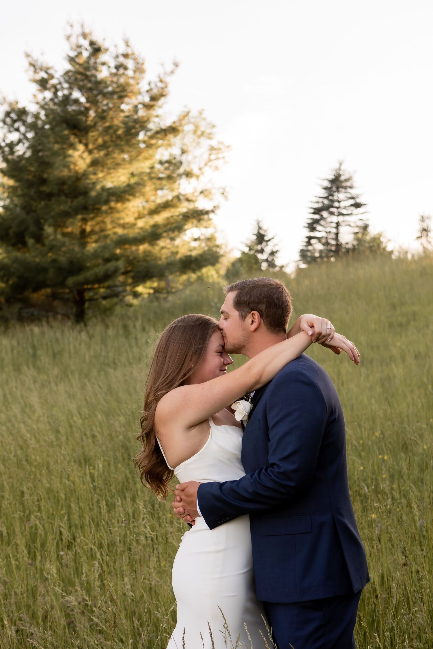 Groom kissing bride's forehead while she hugs him in grassy field in Columbus Ohio