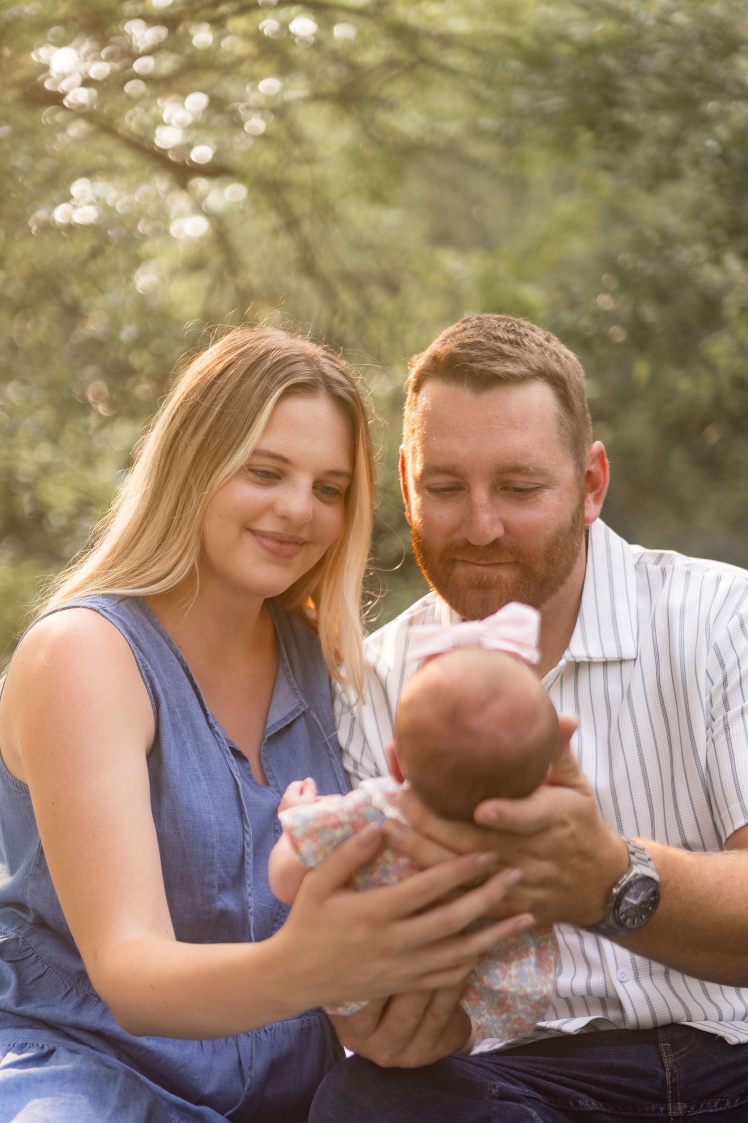 Mother and father looking down and smiling at their newborn baby in a park in Columbus Ohio