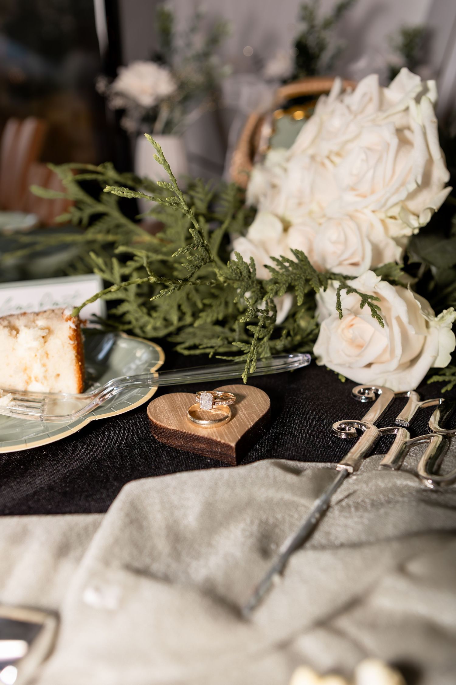 Wedding rings on wooden heart surrounded by bouquet of white flowers, table runner, cake, and other items at wedding in Columbus Ohio