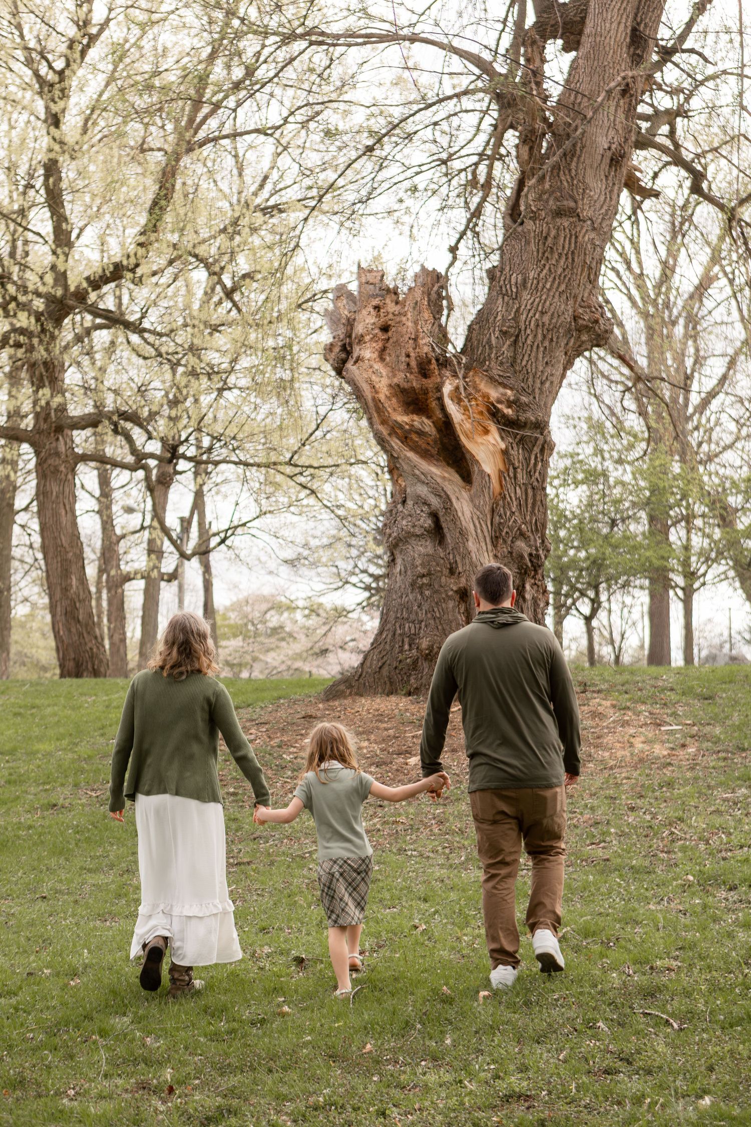 Family of three walking away towards a tree wearing green and white and brown in a park in Columbus Ohio