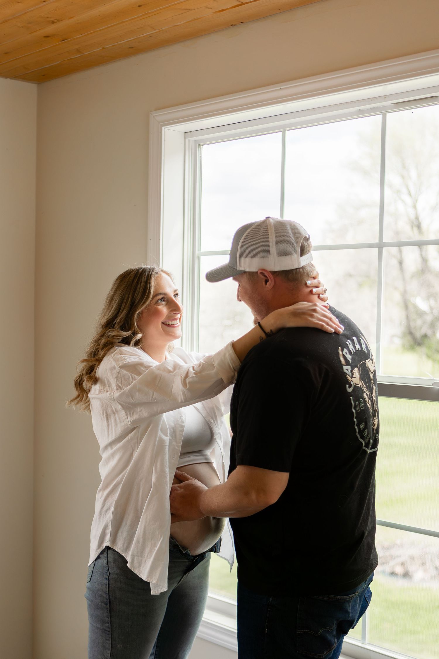 Husband and wife standing in front of window embracing baby bump for maternity photos in Columbus Ohio