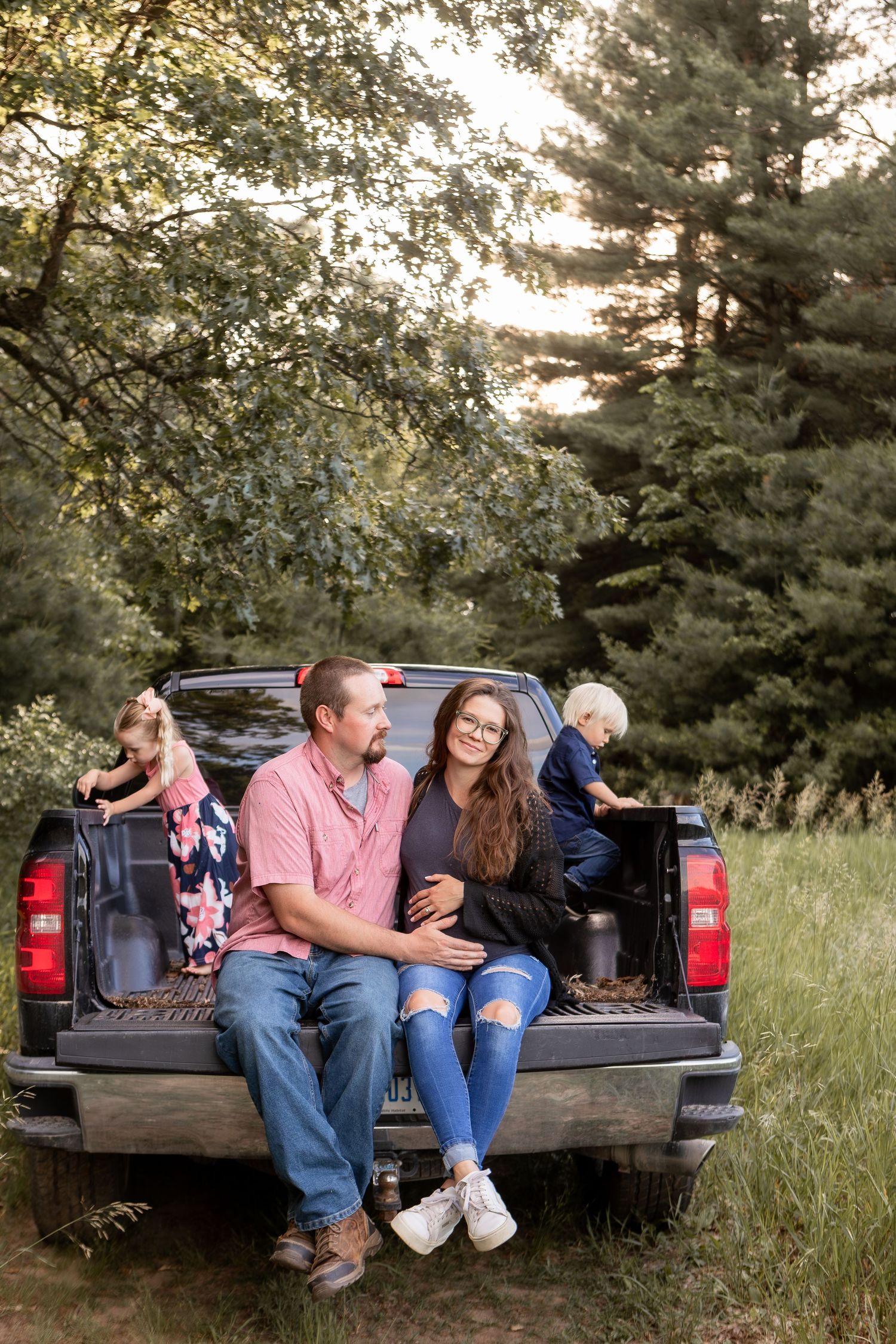 Husband and wife sitting on tailgate of pickup truck with kids playing in truck bed in wheat field in Columbus Ohio