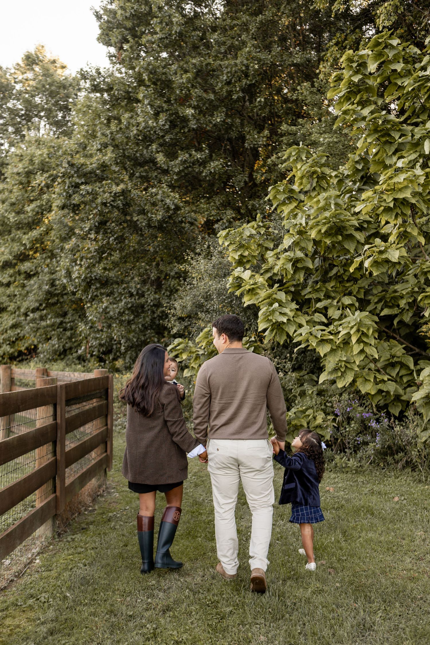 Family of four wearing English style clothing walking beside fence with forest in the background in New Albany Ohio