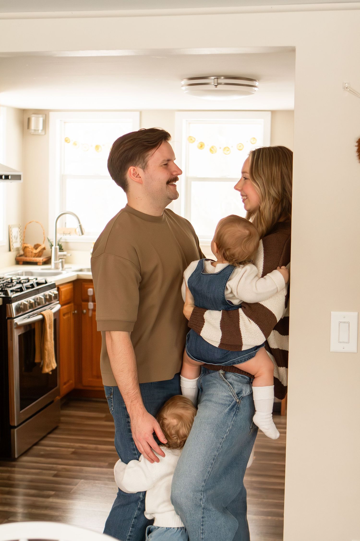 Family of four standing in their kitchen holding their babies smiling in Columbus Ohio