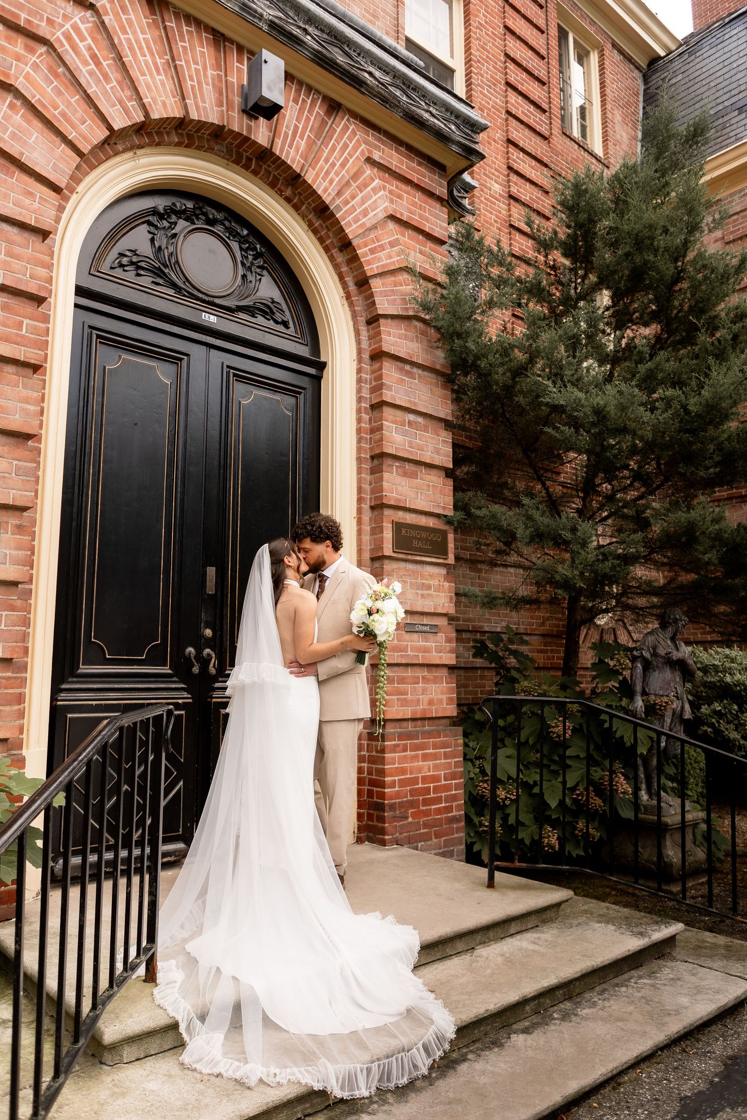 Bride and groom kissing in front of black doors on steps up to a brick building in Mansfield Ohio