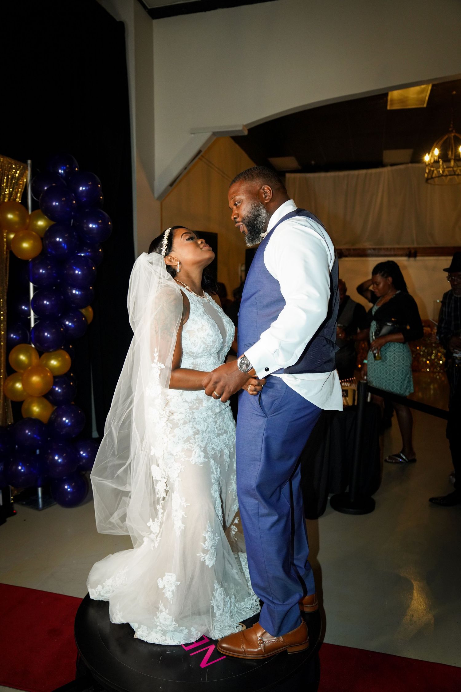 A bride and groom share a romantic dance at their wedding reception, decorated with blue and gold balloons.