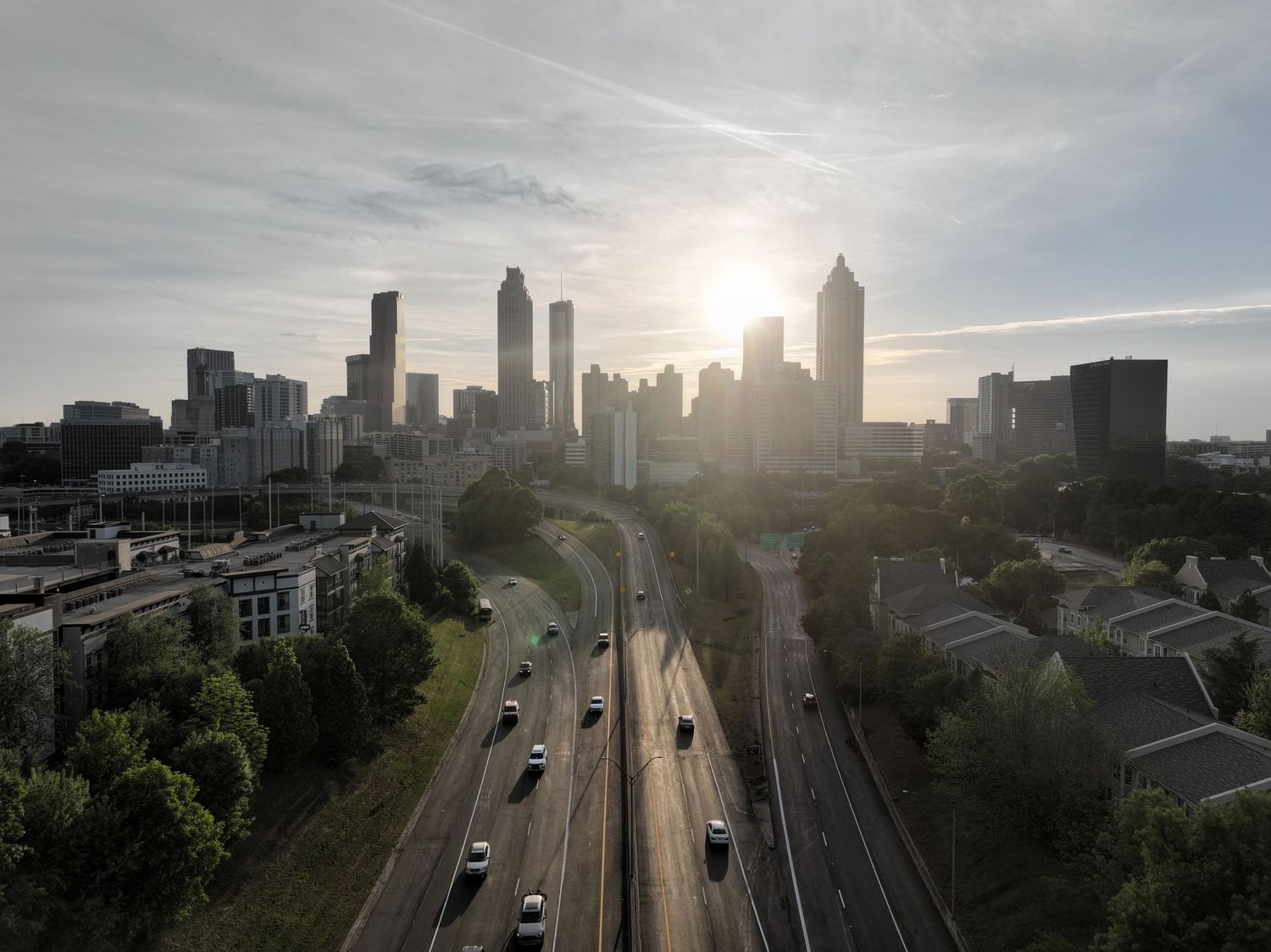 Aerial view of Atlanta skyline at sunset with highway traffic and lush green trees in the foreground.
