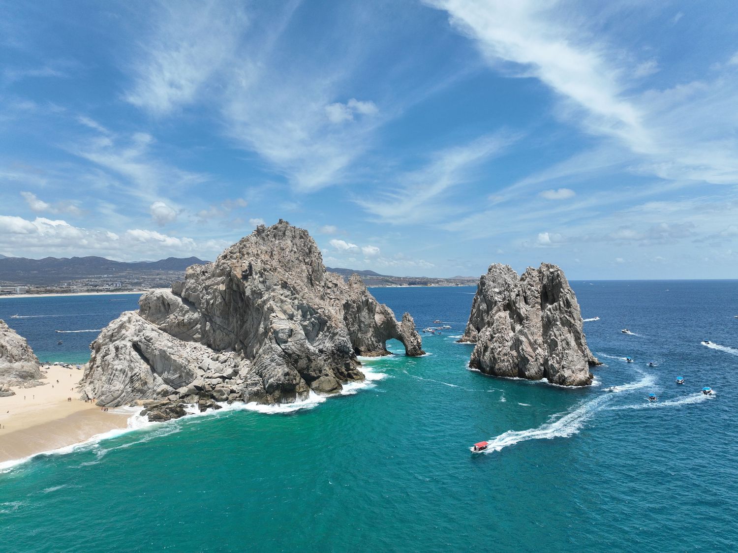 Aerial view of El Arco rock formation in Cabo San Lucas, Mexico, with turquoise waters and a speedboat nearby.