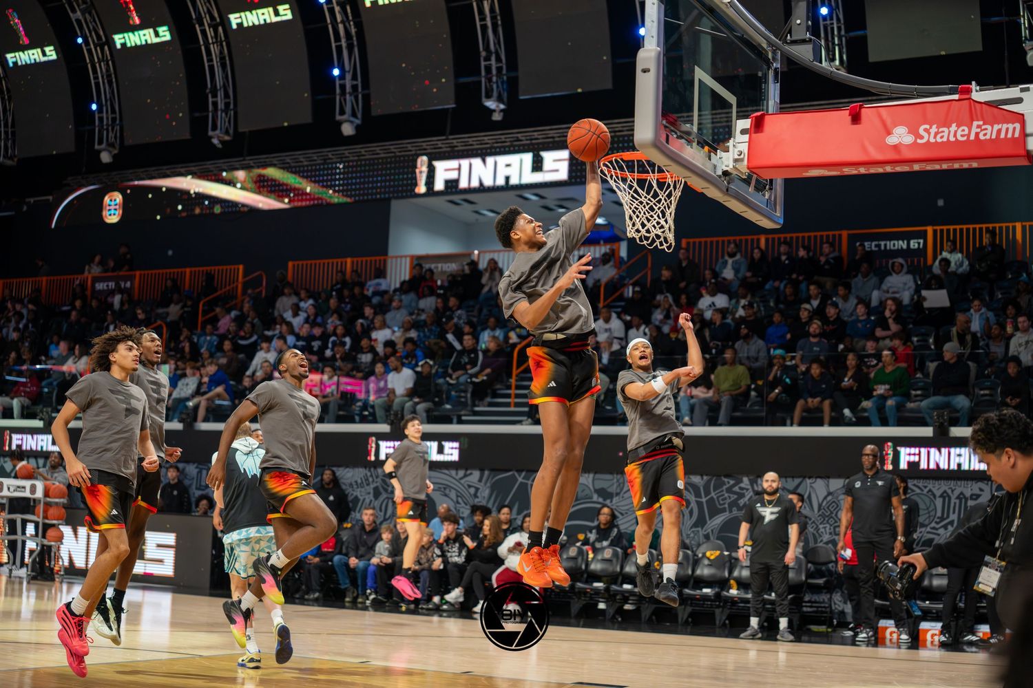 Overtime Elite Finals warmup with player dunking basketball in arena, teammates watching courtside under State Farm signage.