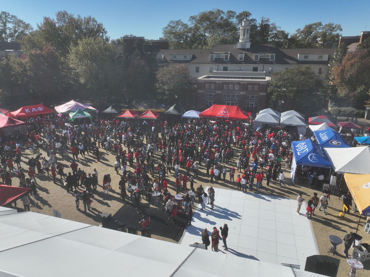Aerial view of a crowded outdoor festival with red tents and vendors on a college campus plaza on a sunny fall day.