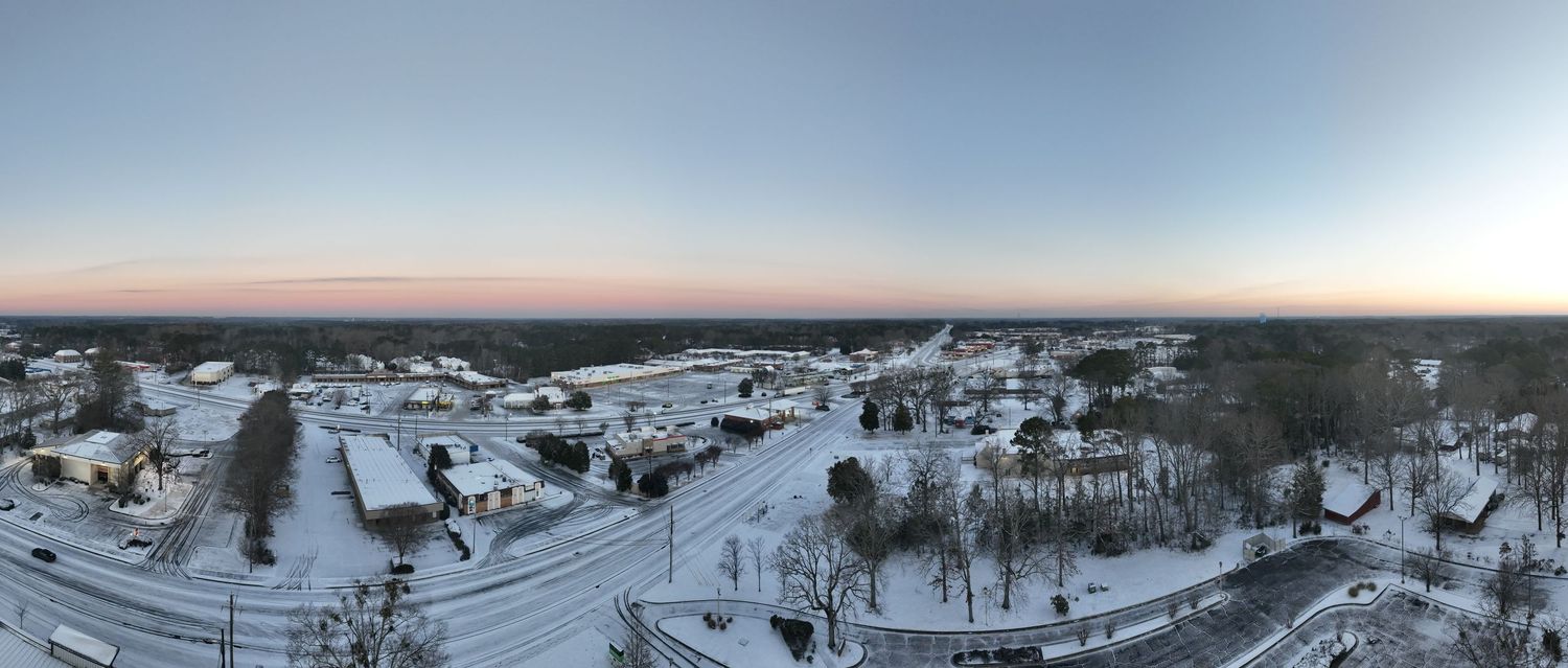 Aerial panoramic winter view of a snow-covered small town at dusk with pink sky on the horizon.