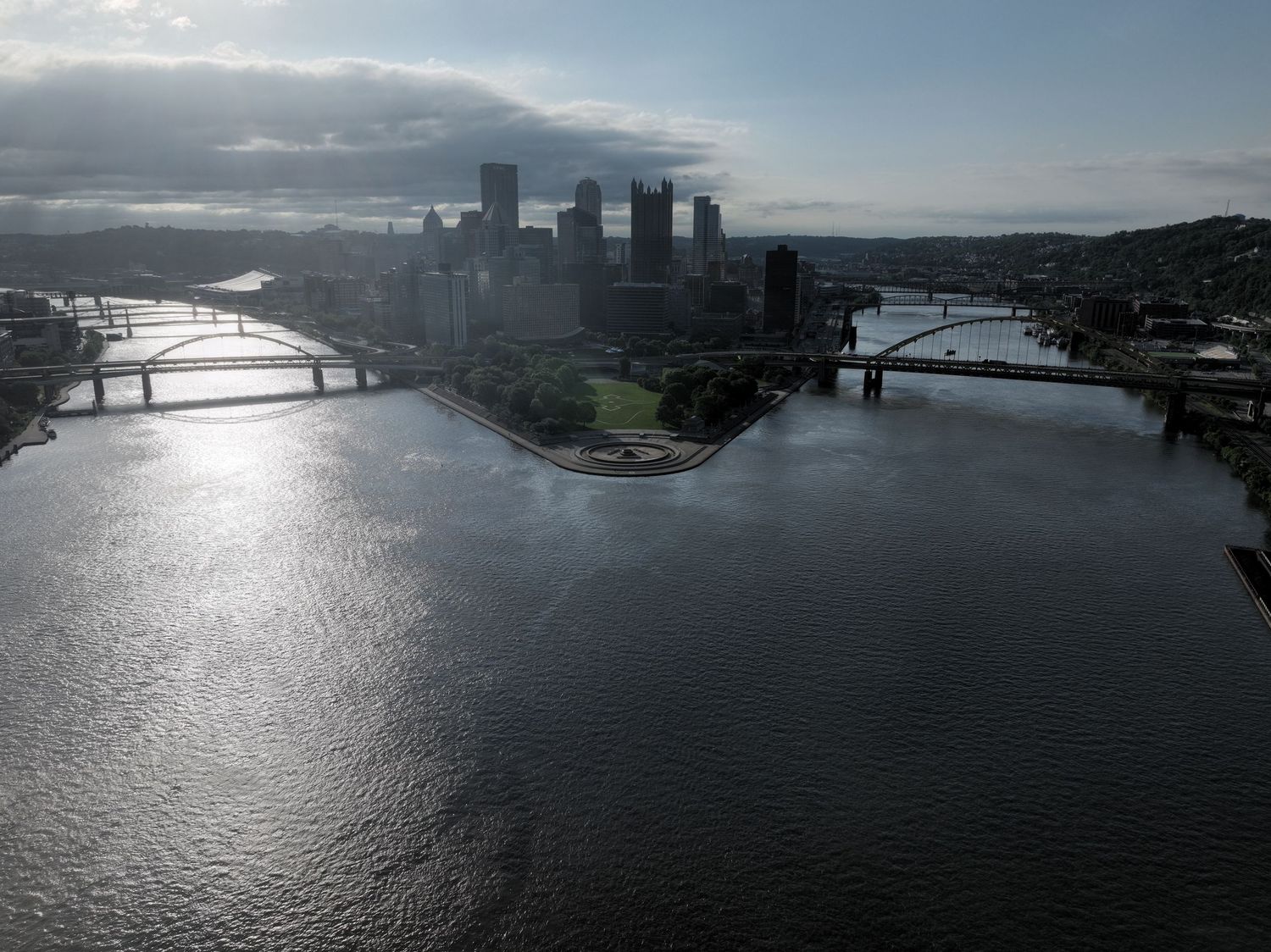 Aerial view of Pittsburgh skyline at the confluence of rivers with bridges spanning the water on a cloudy day.