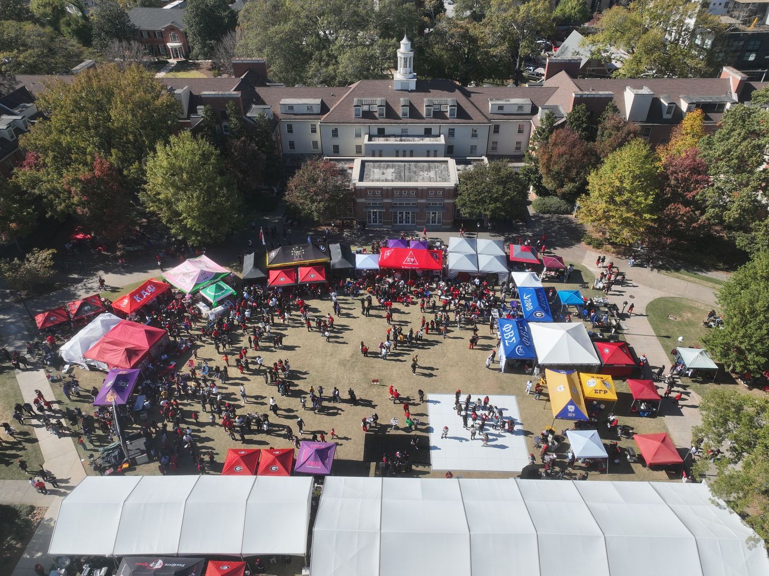 Aerial view of a vibrant outdoor festival with colorful tents and crowds on a sunny day near a historic building.