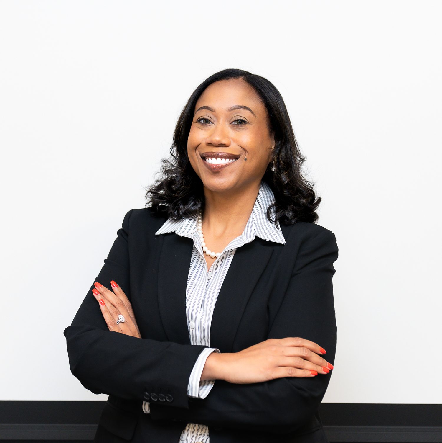 Professional woman in black blazer smiling confidently with arms crossed against white background.