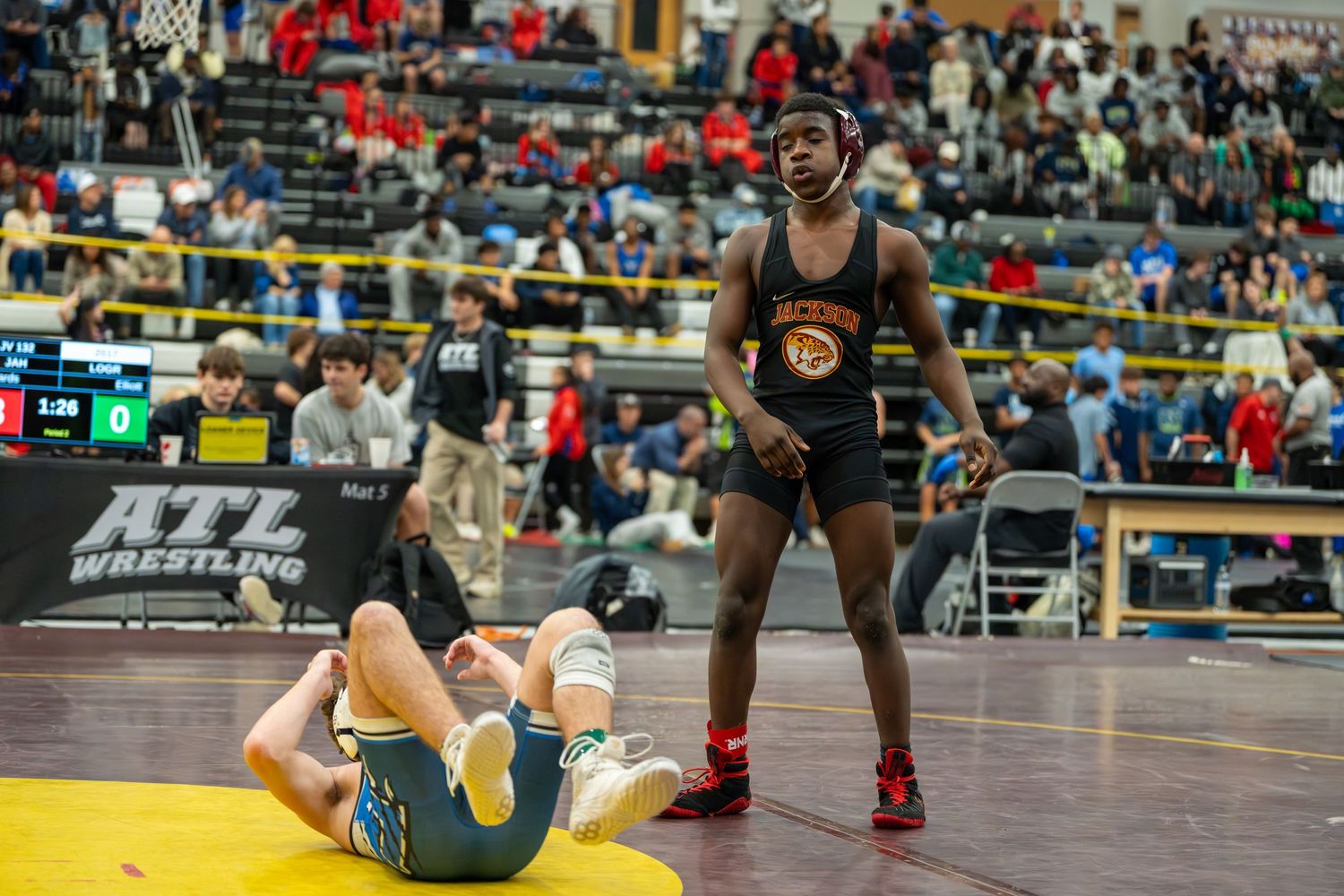 Wrestler in black uniform stands victorious over opponent on mat at ATL Wrestling tournament competition.