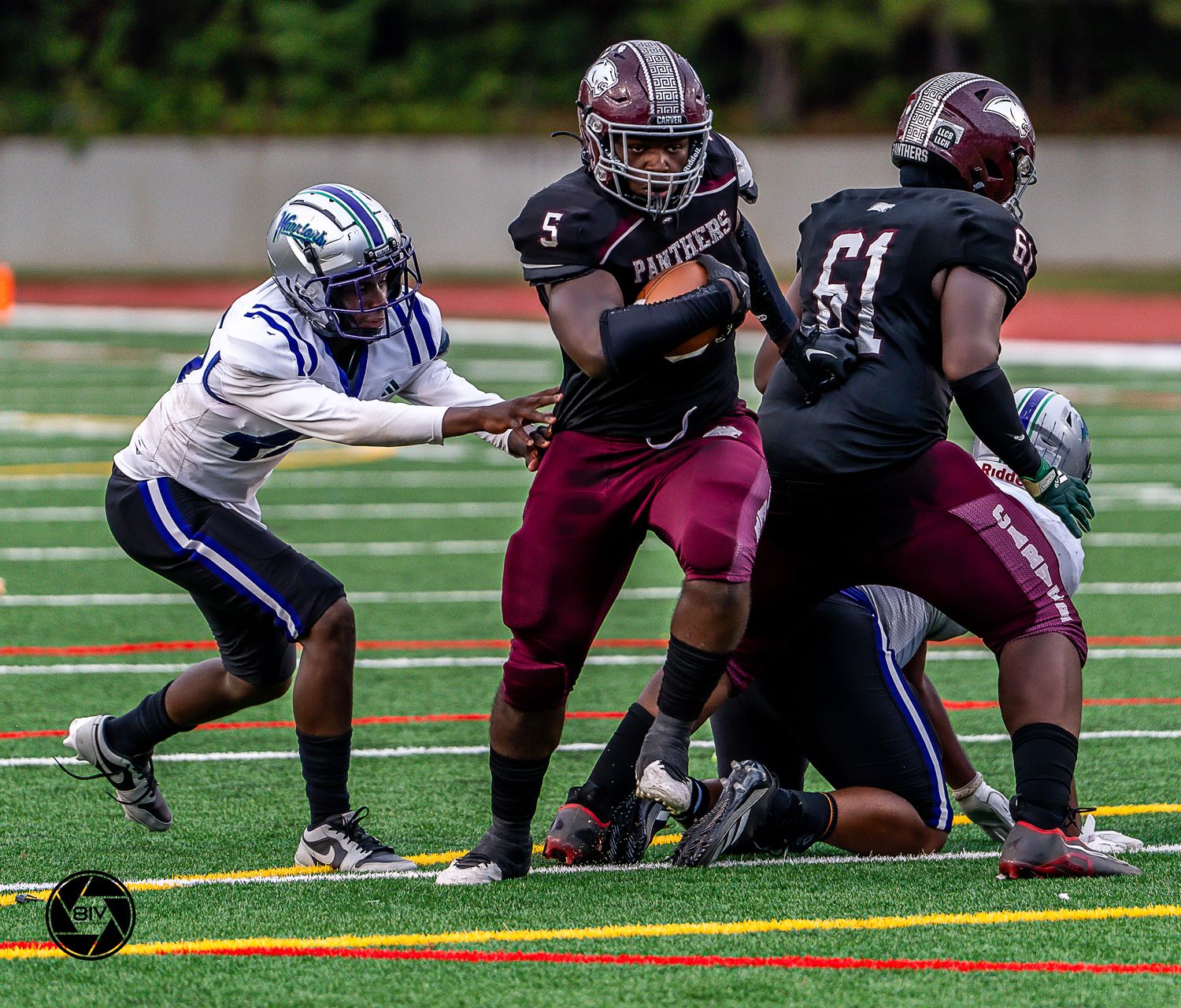 High school football players in maroon Panthers uniforms compete against blue-uniformed opponents on a green turf field.