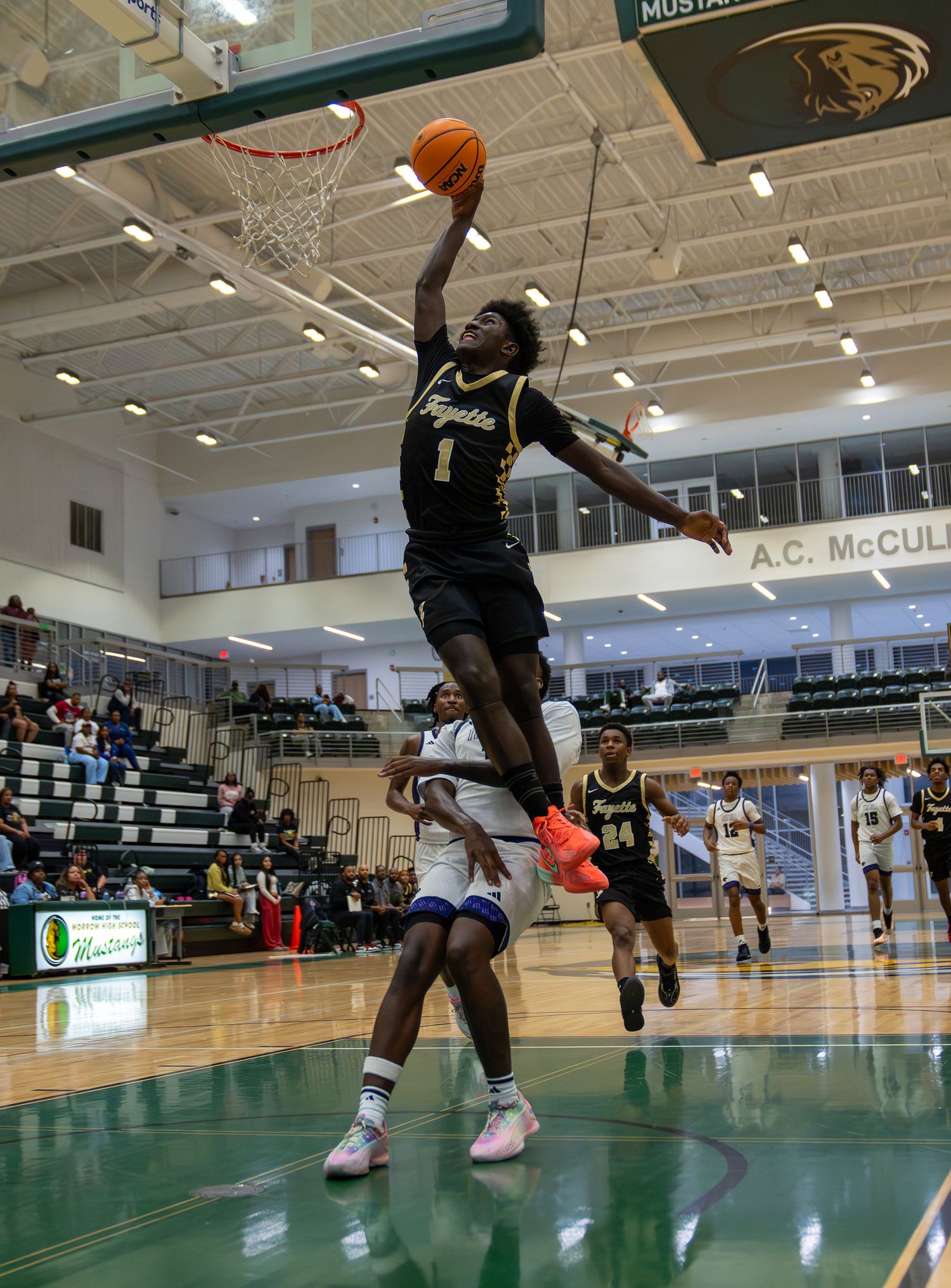 Player #1 in black uniform leaps for a slam dunk during a high school basketball game.