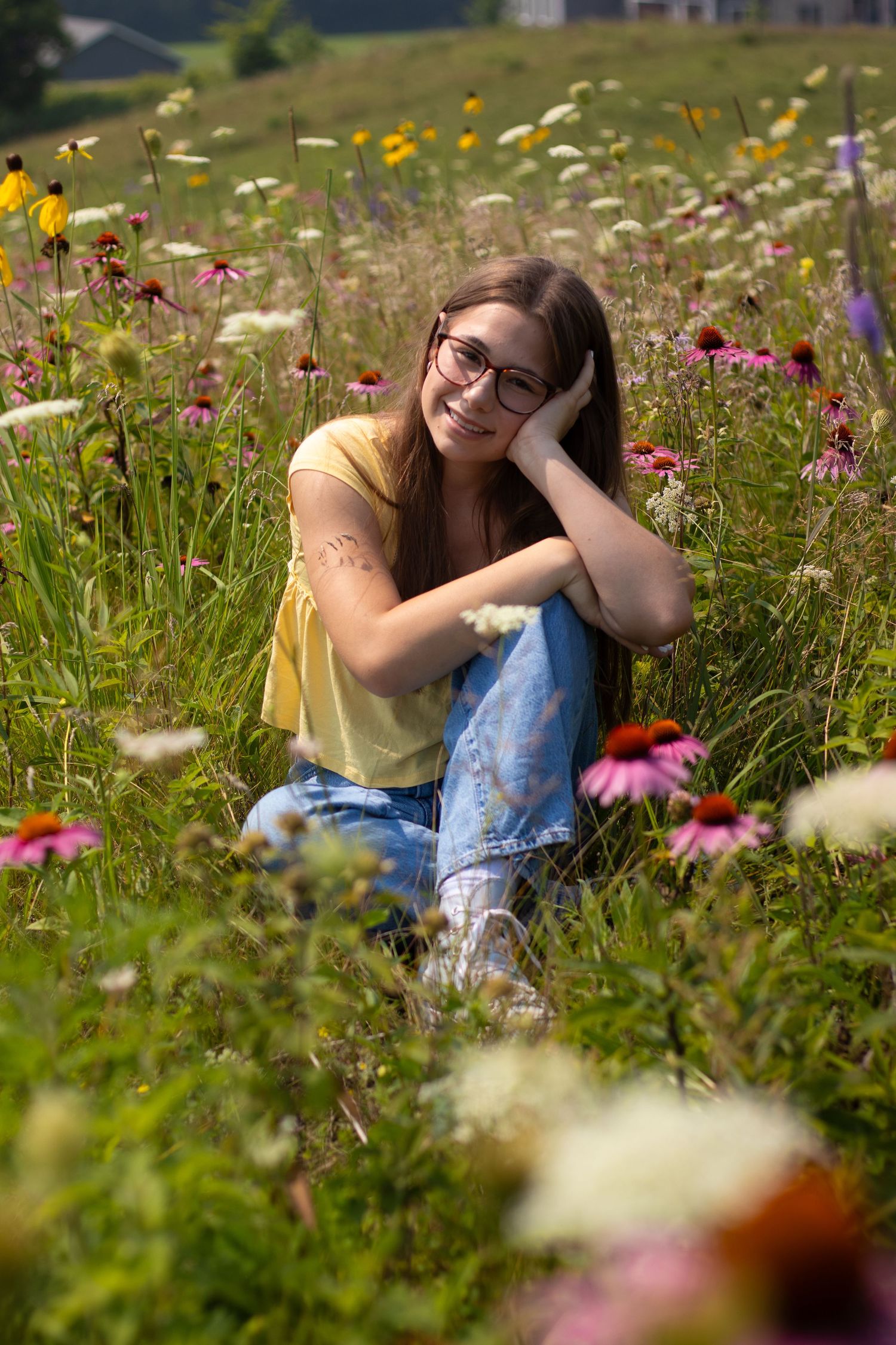 Smiling teenage girl with glasses sitting in a colorful wildflower meadow.