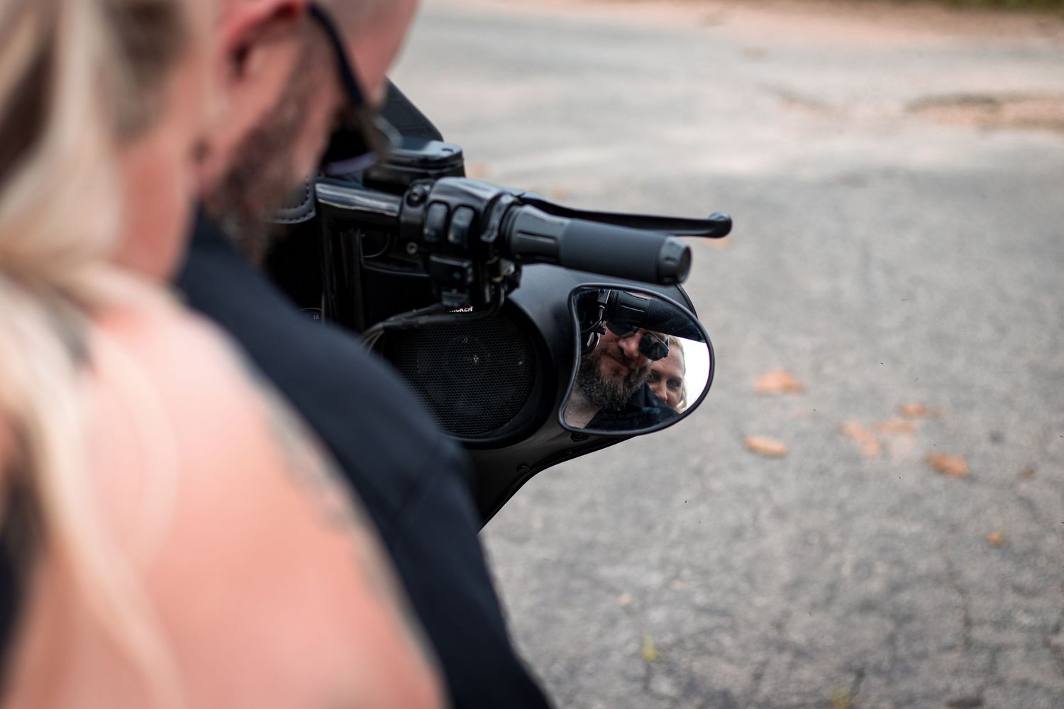 Couple reflected in motorcycle mirror on a road.