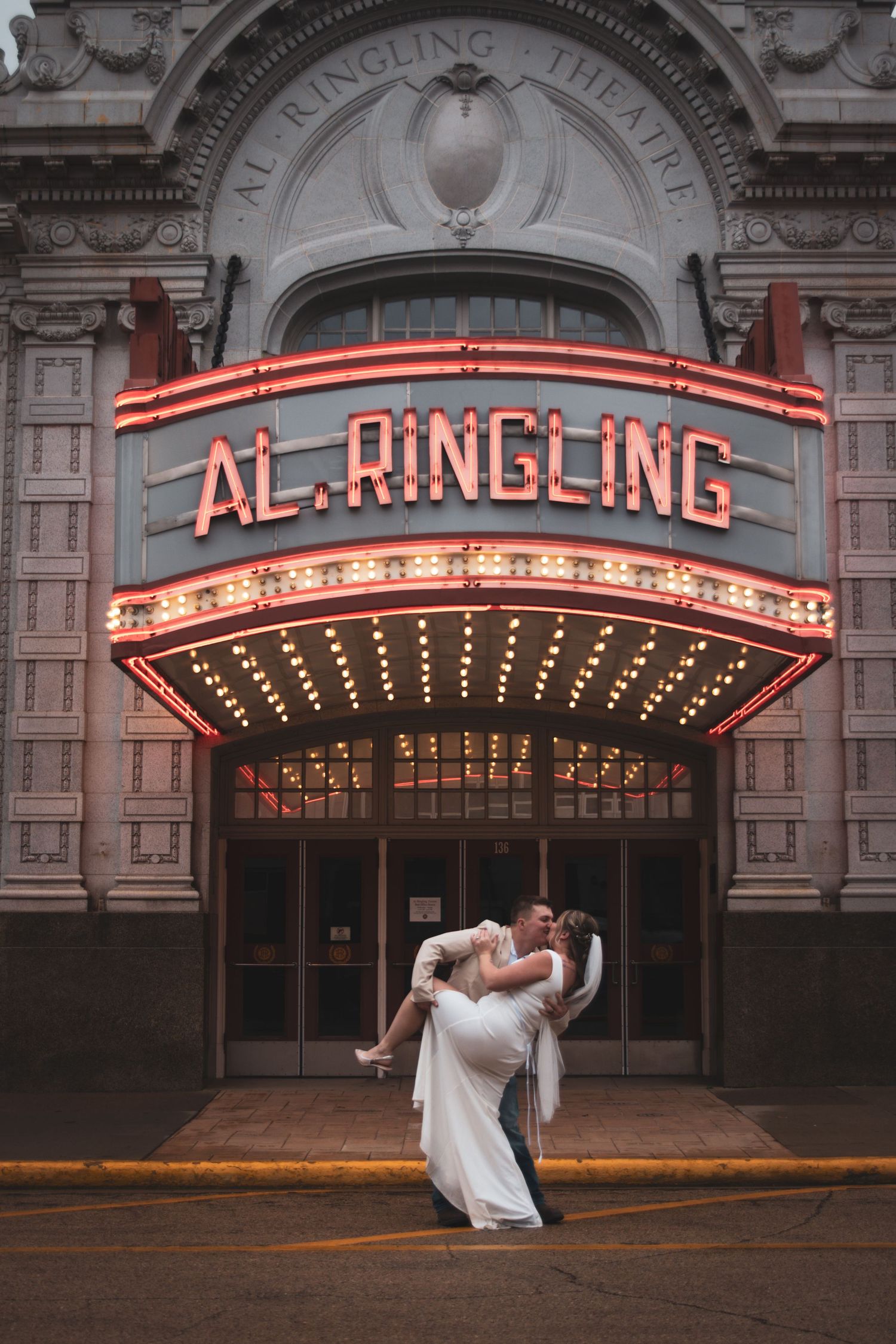 Couple sharing romantic dip kiss under glowing Al. Ringling Theatre marquee sign at night.
