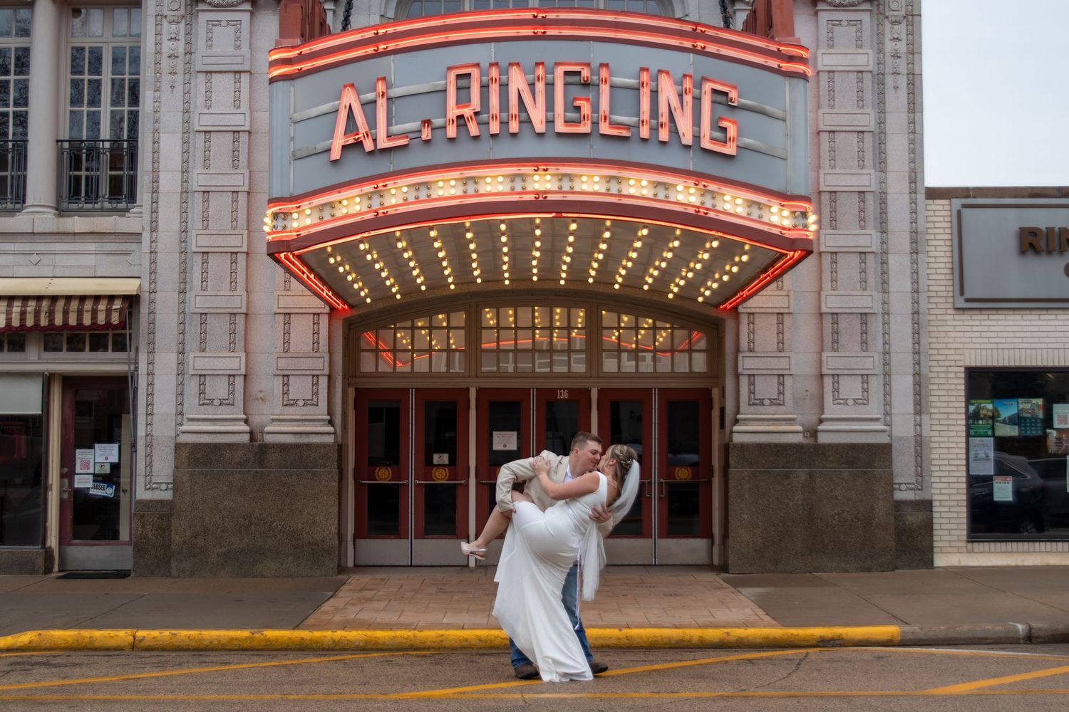Couple shares romantic dip kiss in front of the illuminated Al. Ringling Theatre marquee sign.