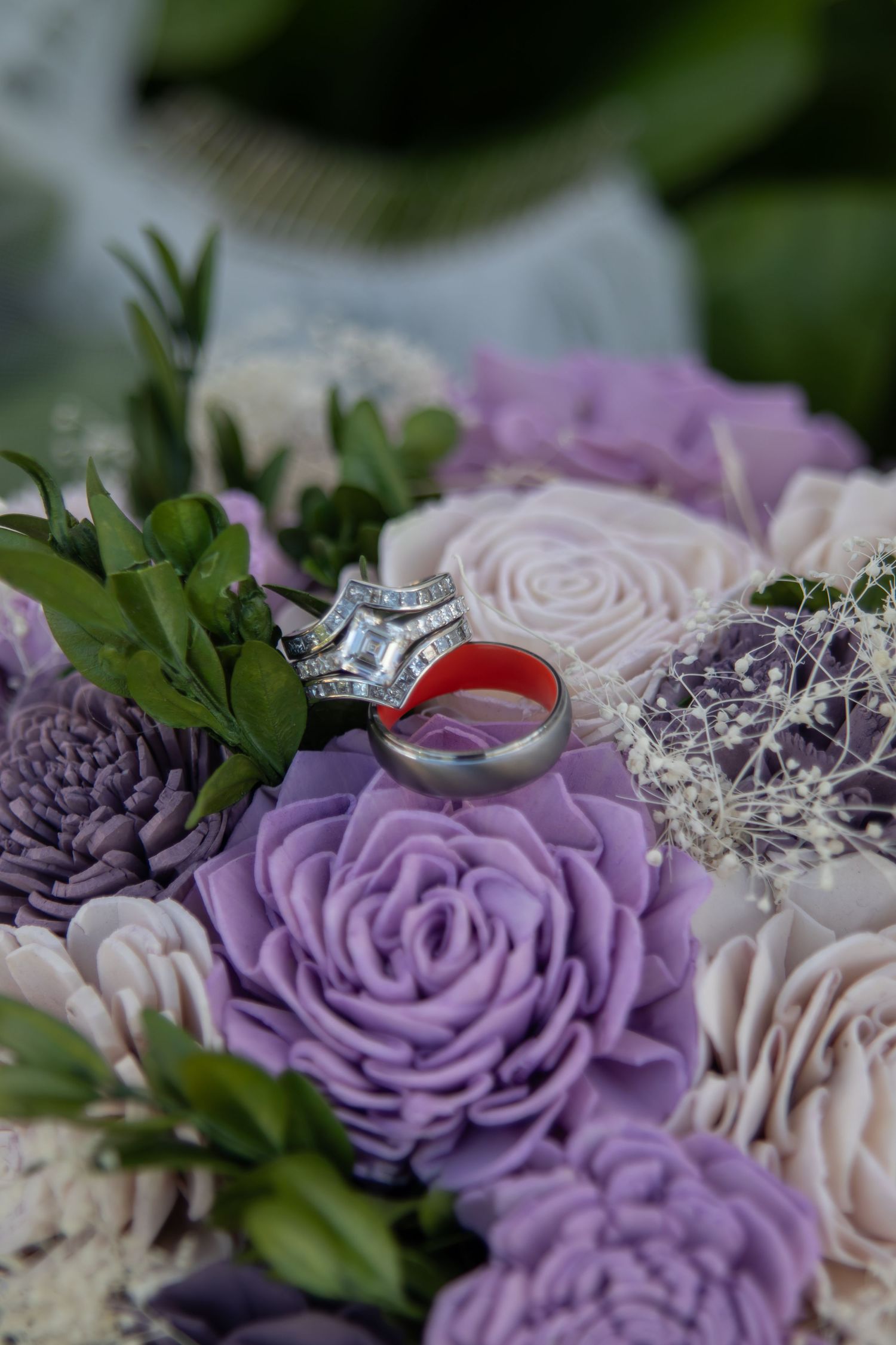 Wedding rings resting on a bouquet of purple and blush roses with green foliage.