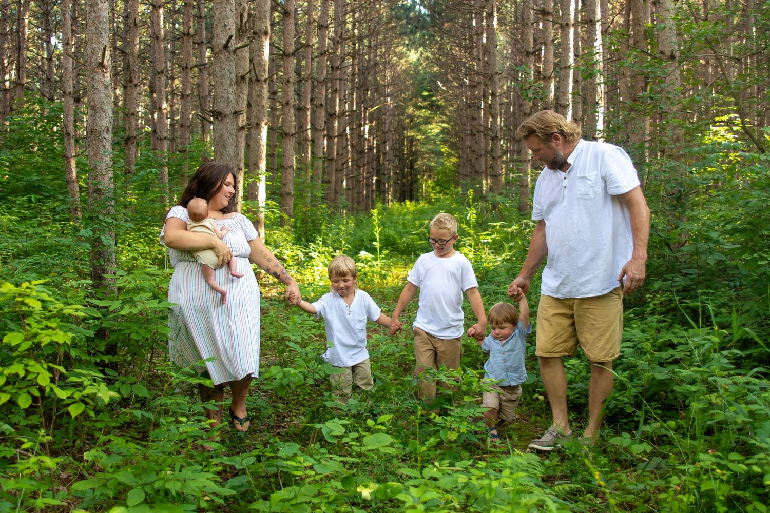 Family with newborn and children walking through a lush green forest on a sunny day.