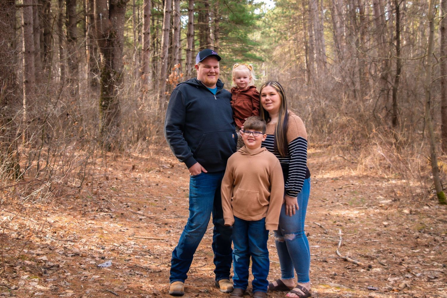 Family of four posing on a wooded forest path during early spring season.