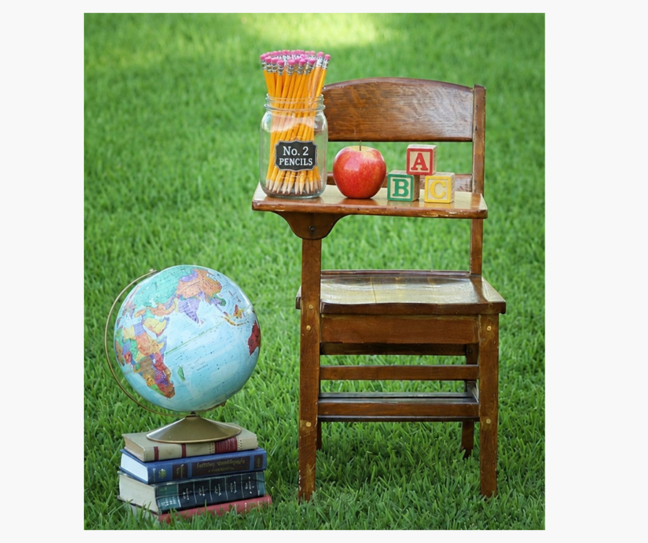Vintage wooden school desk with ABC blocks, apple, No. 2 pencils jar, and globe on stacked books outdoors.
