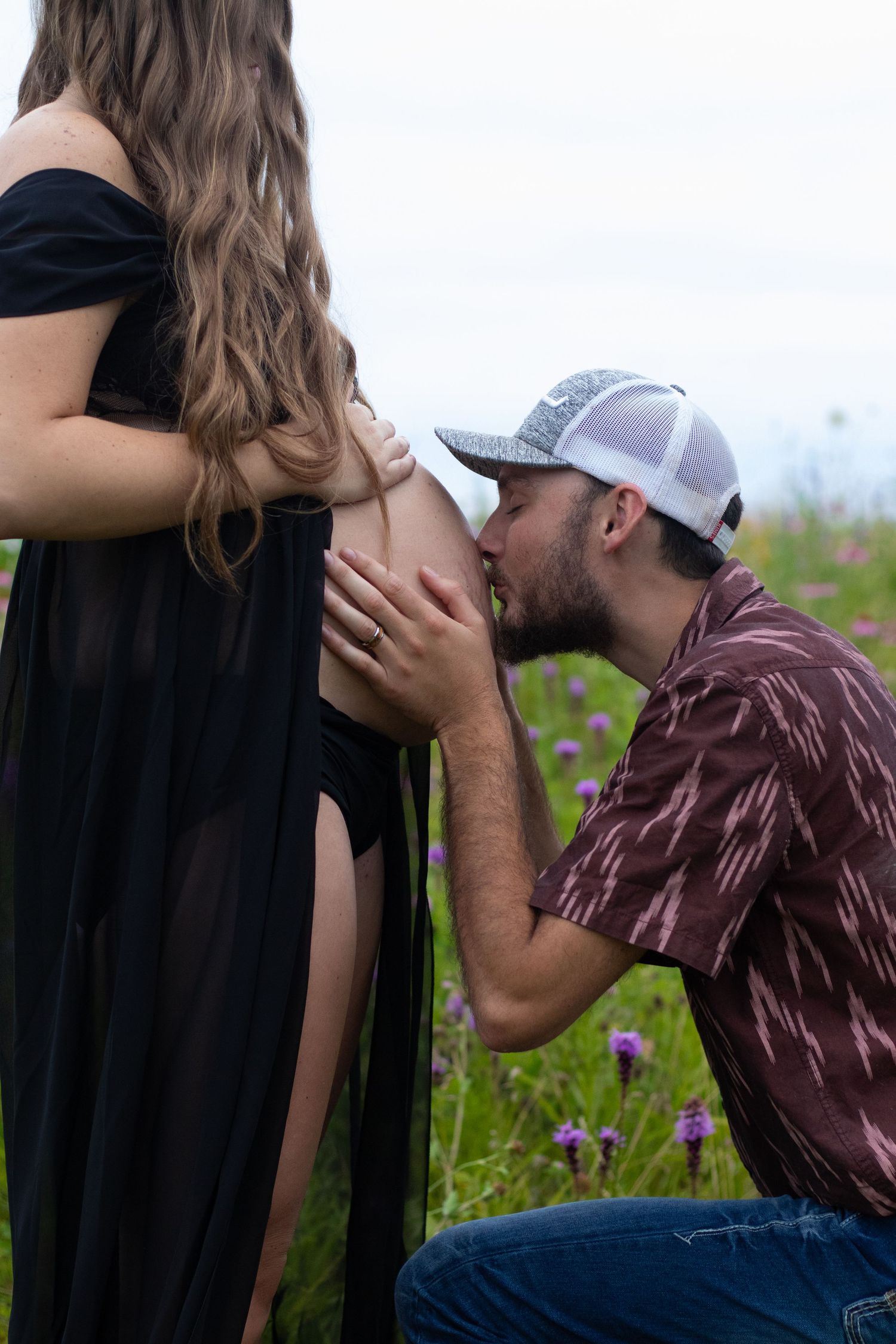 Man kneeling to kiss pregnant woman's belly during outdoor maternity session.