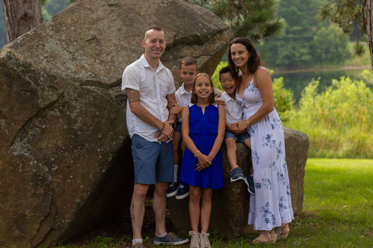 Family of five posing near a large boulder in a lush green park setting during summer.