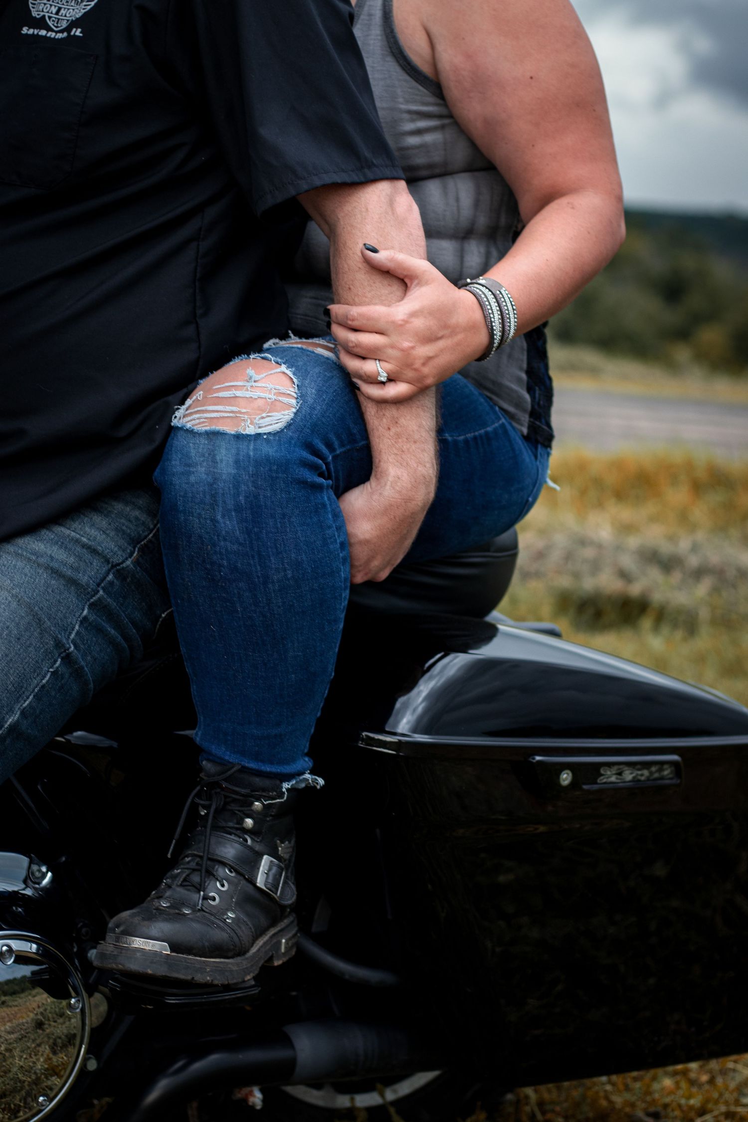 Couple sitting together on Harley Davidson motorcycle on rural roadside on cloudy day.